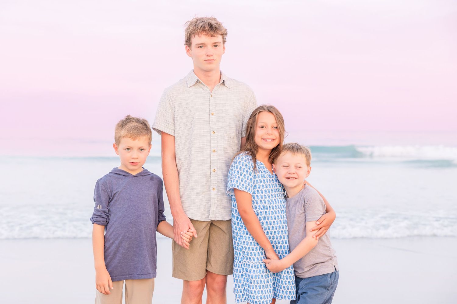 Family group photo on beach with gentle waves and pink sunset sky.
