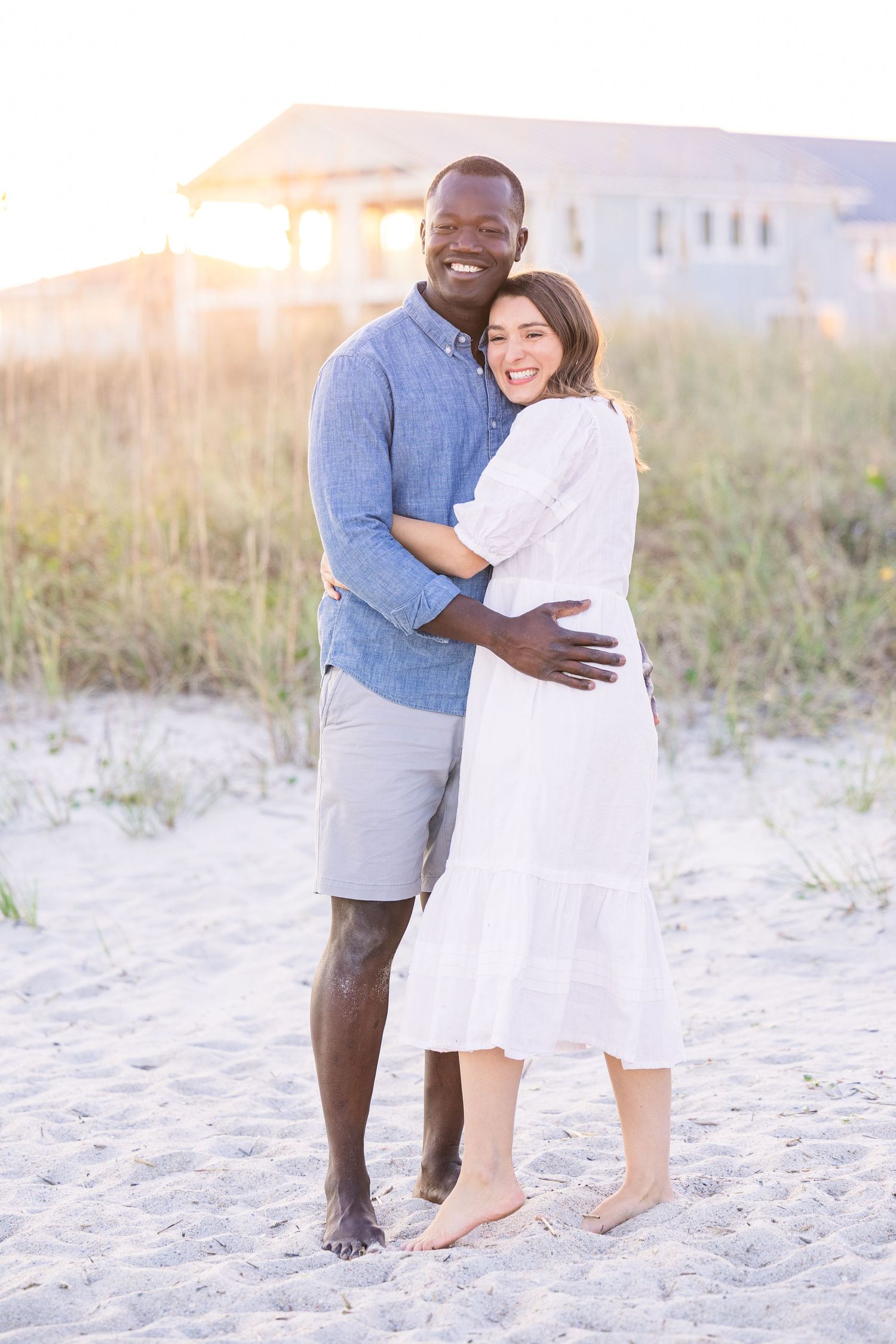 Couple embracing on the beach during sunset with house in background.