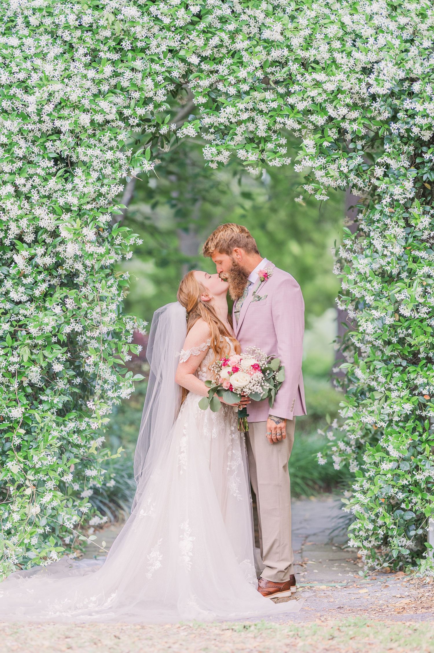 Wedding couple shares romantic moments under canopy of white spring blossoms in garden setting in harborway gardens in Wrightsville Beach