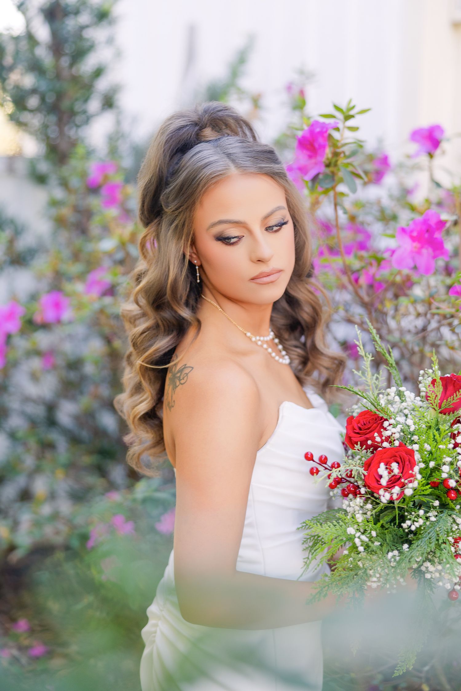 Bridal portrait with pink flowers in background and red bouquet against soft natural lighting.