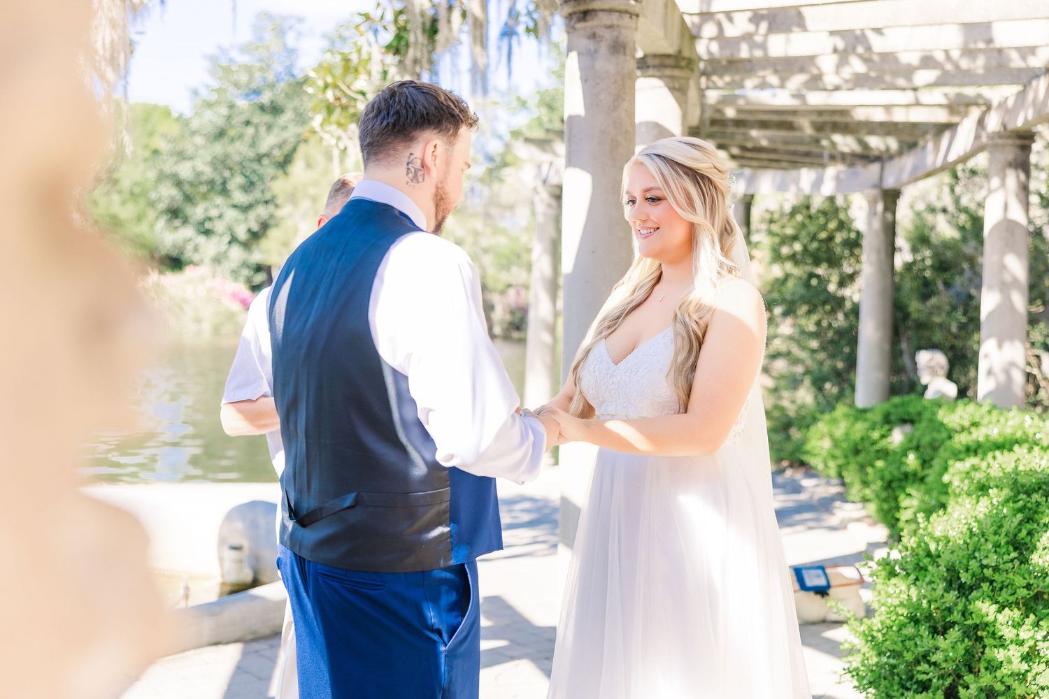 Bride and groom exchange vows outdoors under a pergola, holding hands in a romantic garden wedding ceremony in Airlie Gardens in Wilmington,