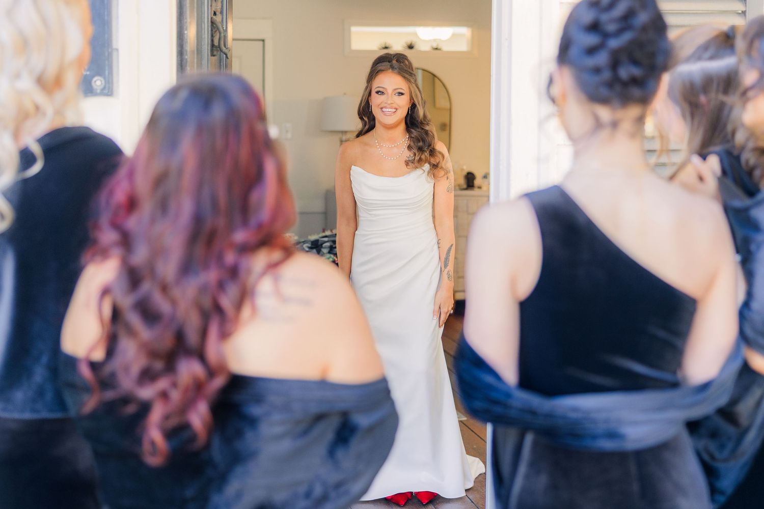 Bride in fitted white gown reveals her dress to attendants in navy dresses.