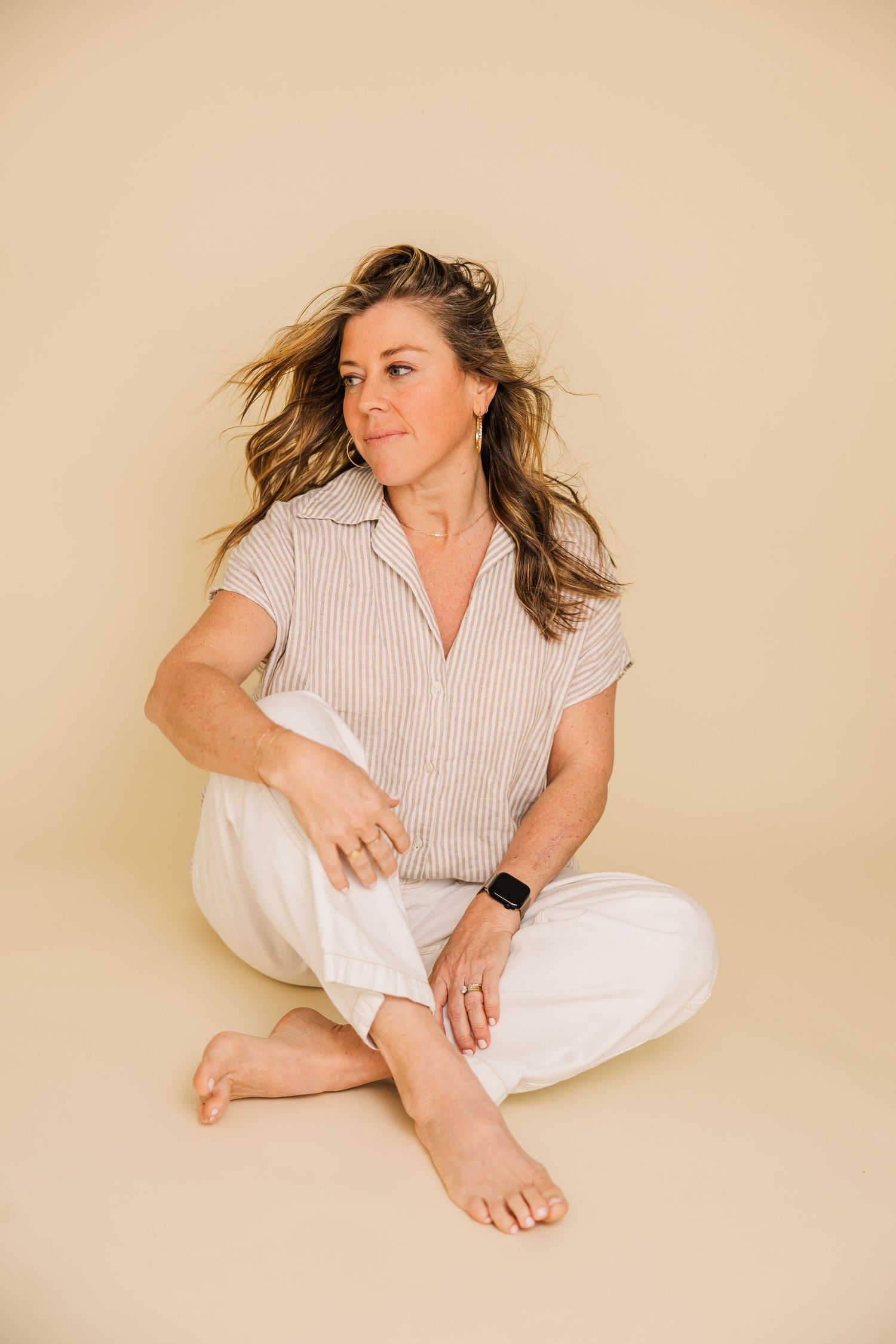 Casual lifestyle portrait of person in white pants and striped shirt sitting on floor.