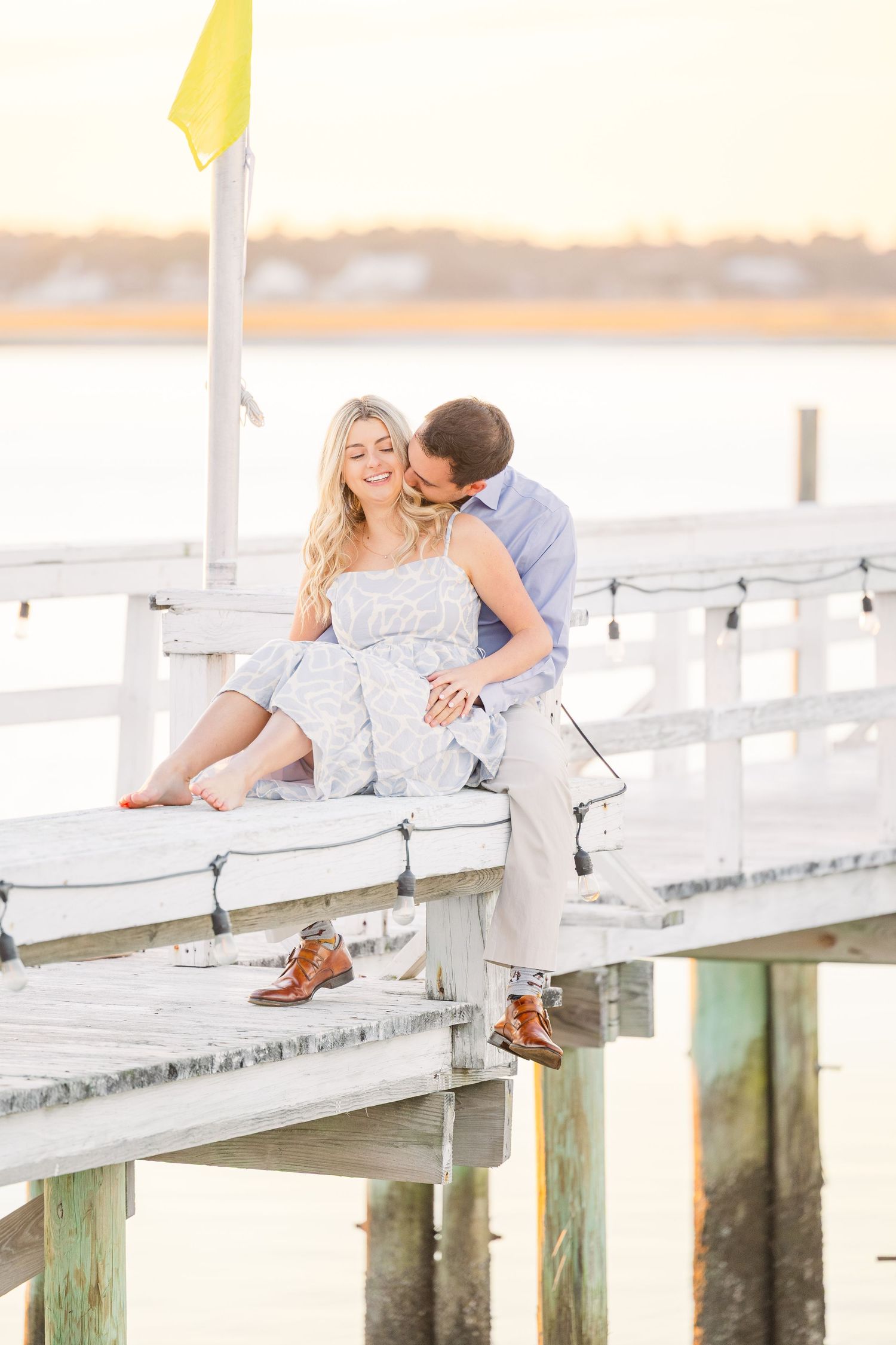 Intimate waterfront moment captured on white pier during sunset with golden lighting.