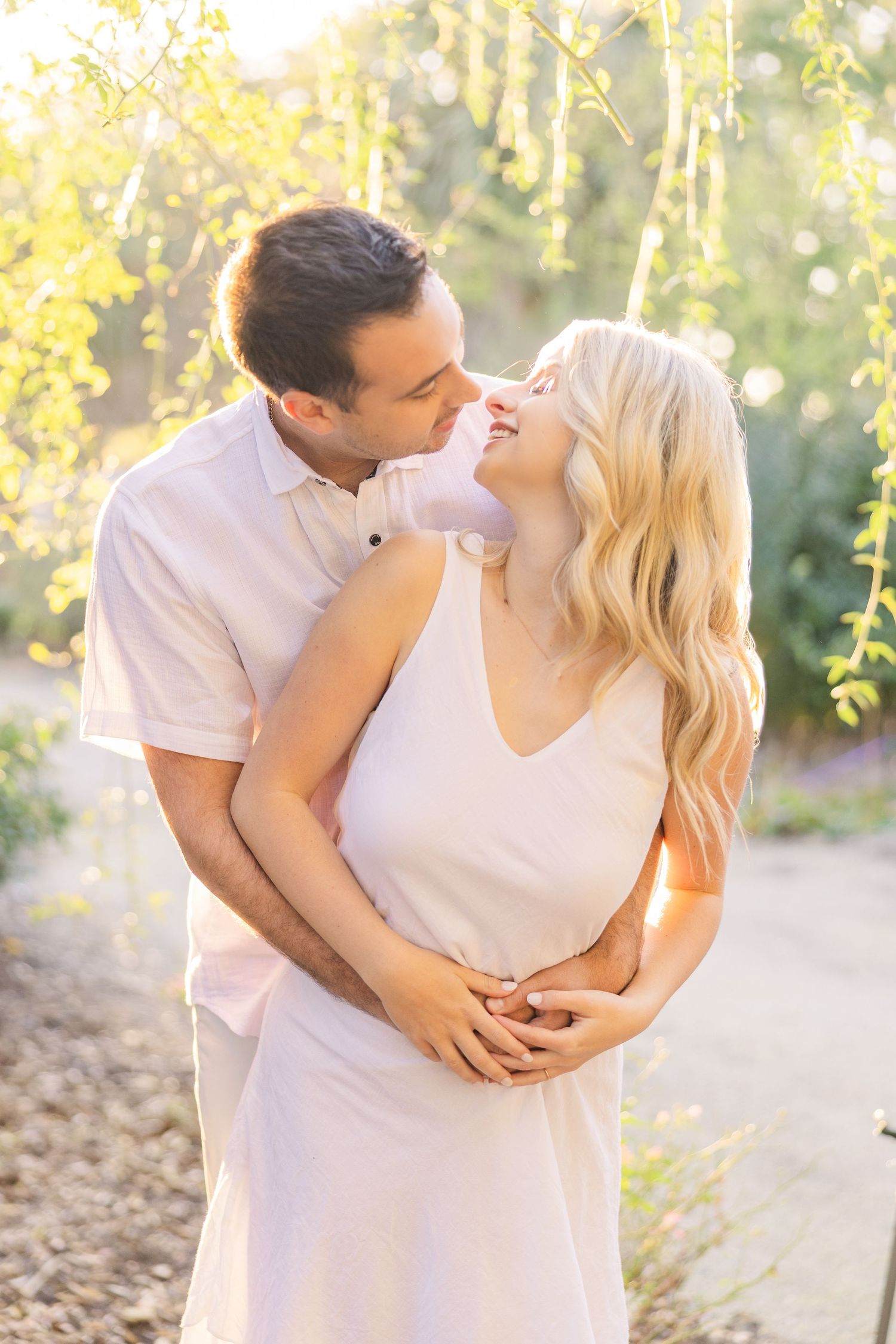 A romantic embrace in a sun-dappled garden with golden light filtering through trees.