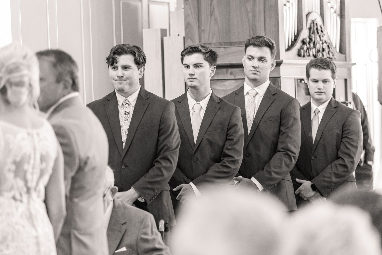 Wedding party members in navy suits and tan suits stand together during an emotional ceremony moment.