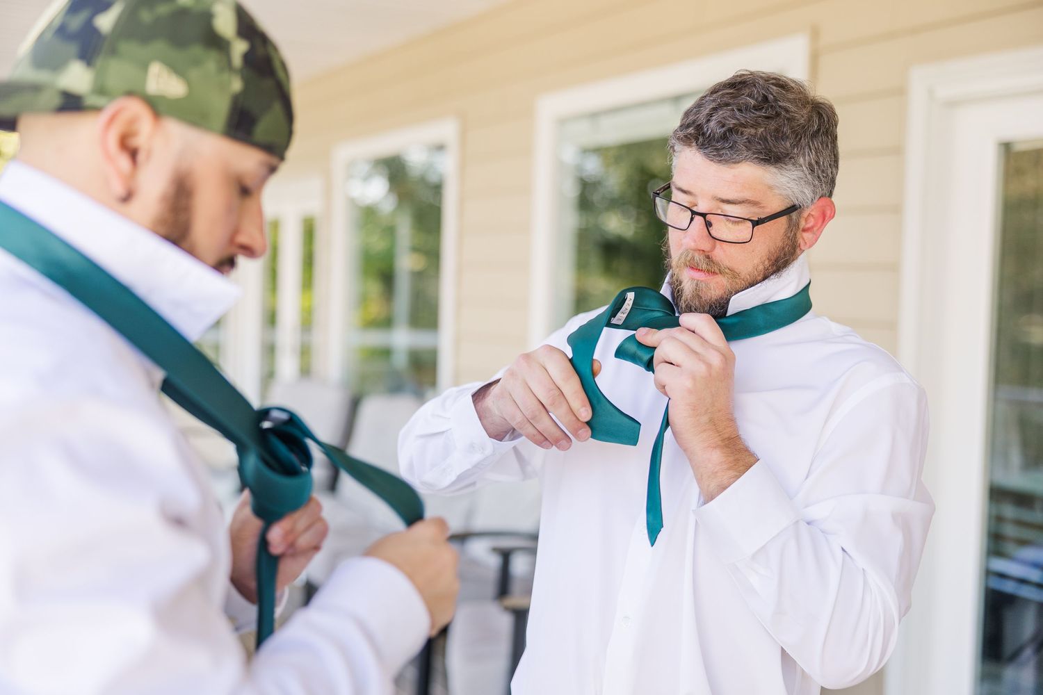 Someone adjusts their tie while standing on an outdoor porch with white columns wedding groom bride lake Gaston photographer light airy