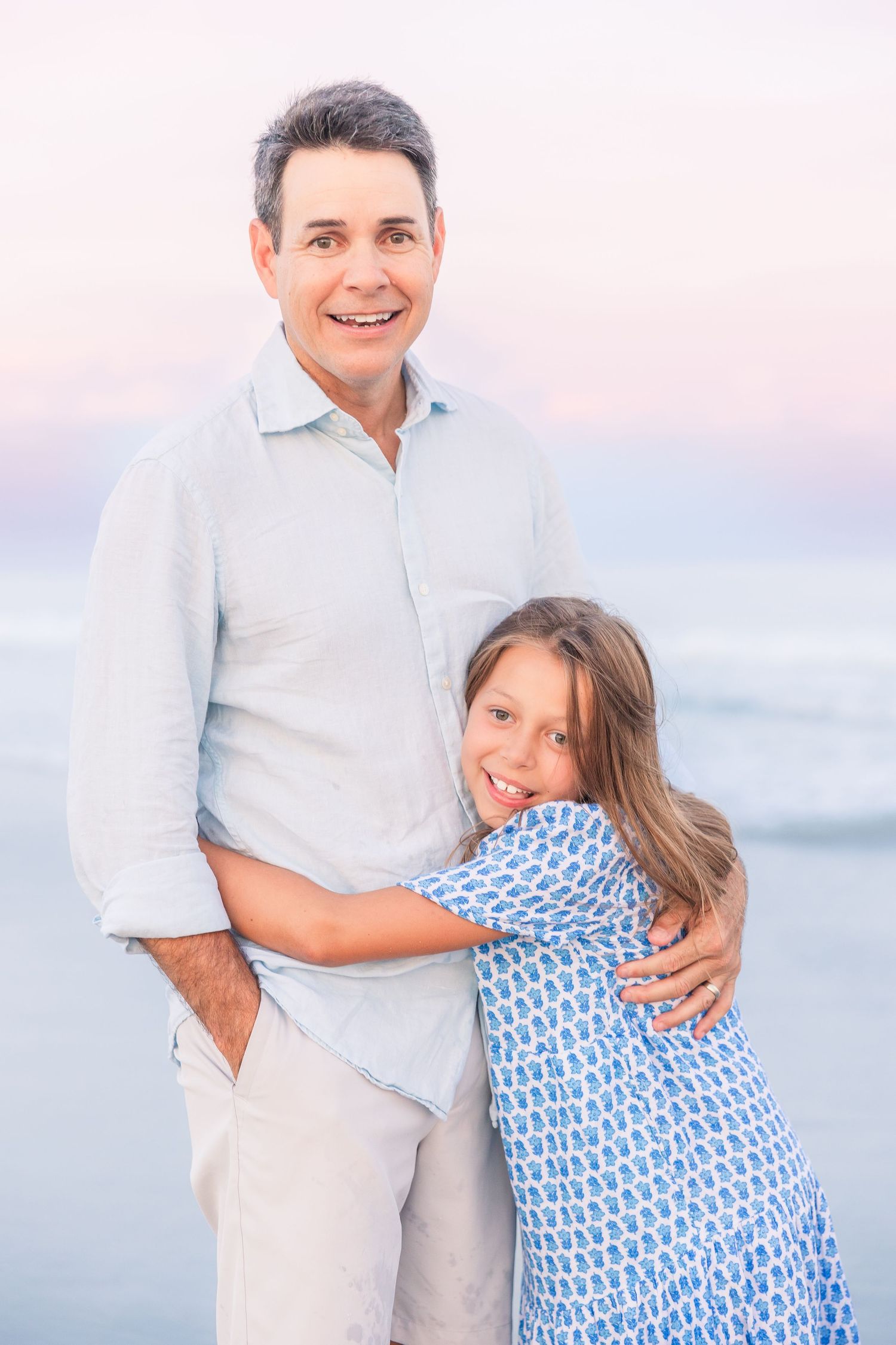 A heartwarming embrace between two people in coordinating blue and white outfits on the beach at dusk.