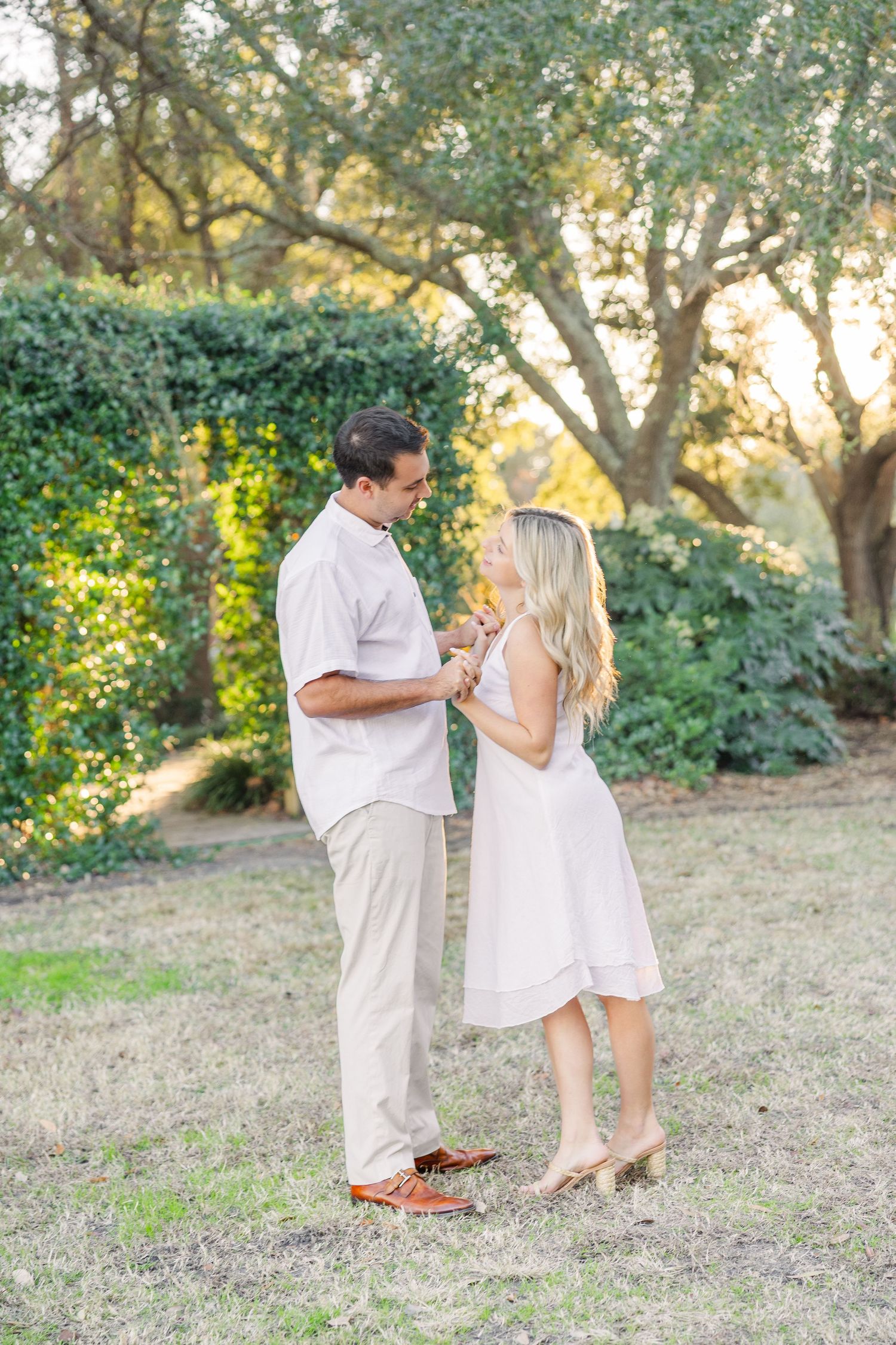 A couple in white outfits shares a romantic moment together in a sunlit outdoor setting.