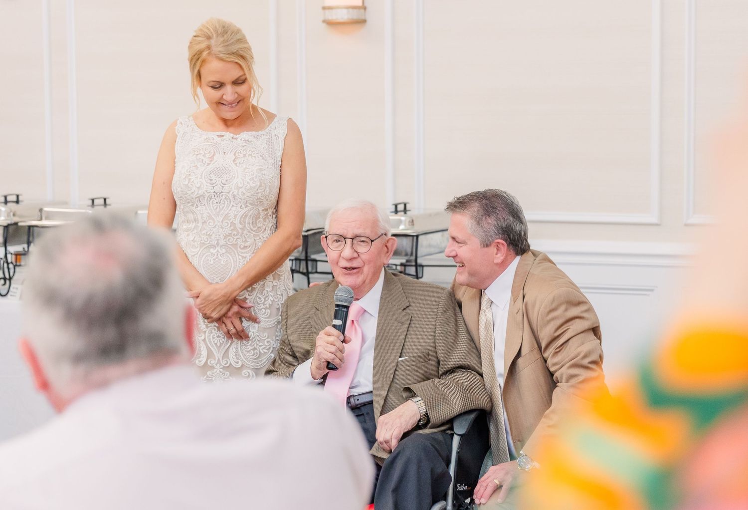 Wedding guests sharing joyful interactions in a bright reception hall with white walls.