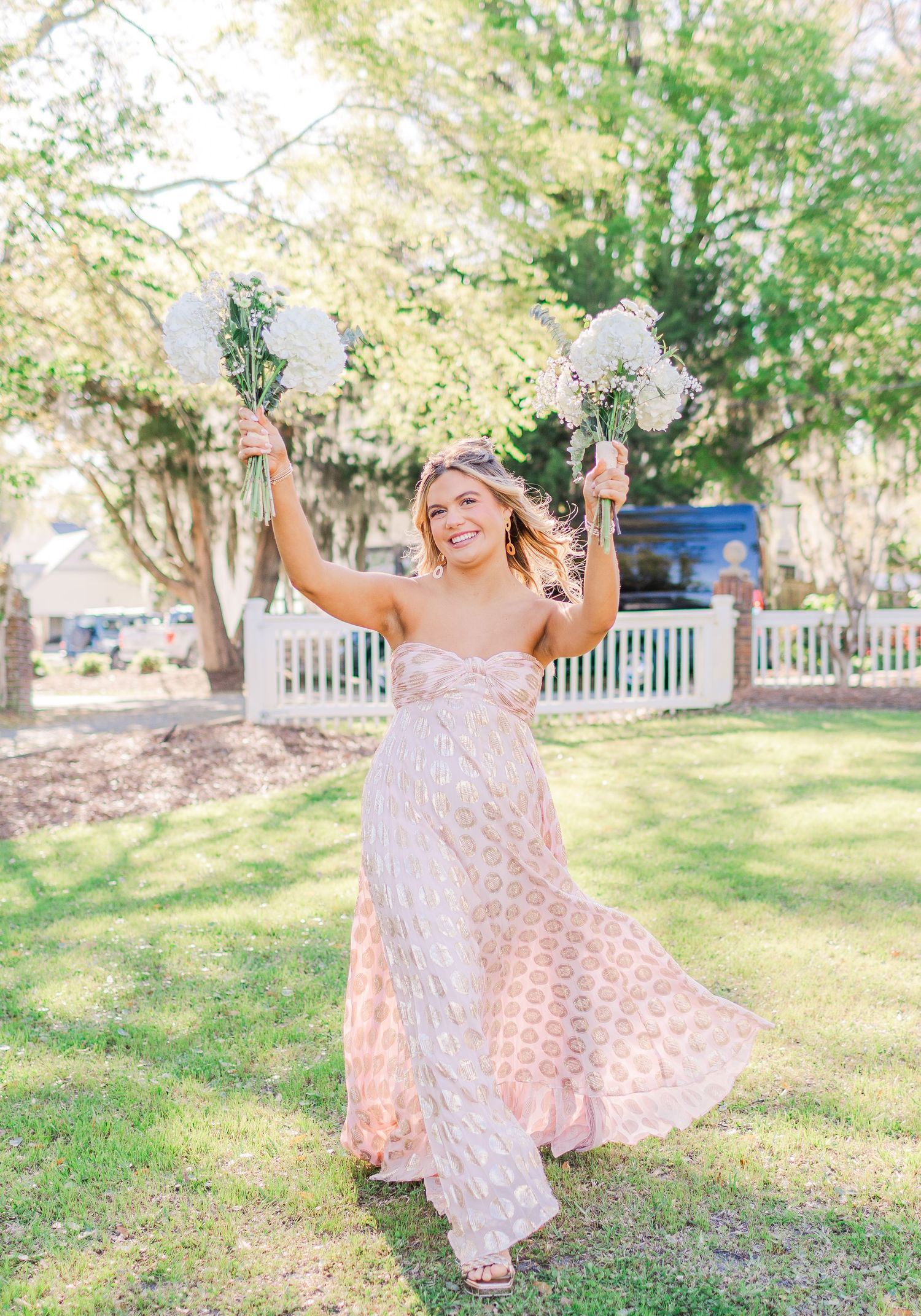 Bride twirling in lace wedding dress during outdoor photo session on sunny lawn.