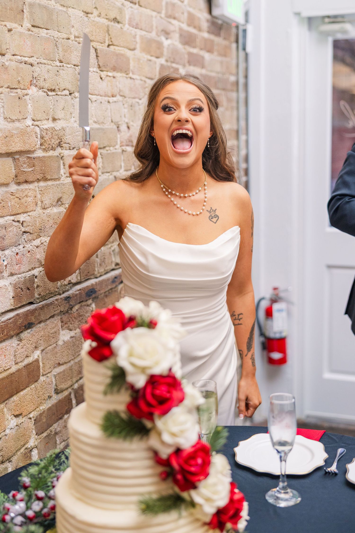 Joyful celebration moment near a wedding cake decorated with red and white roses wedding groom bride wilmington North Carolina photographer