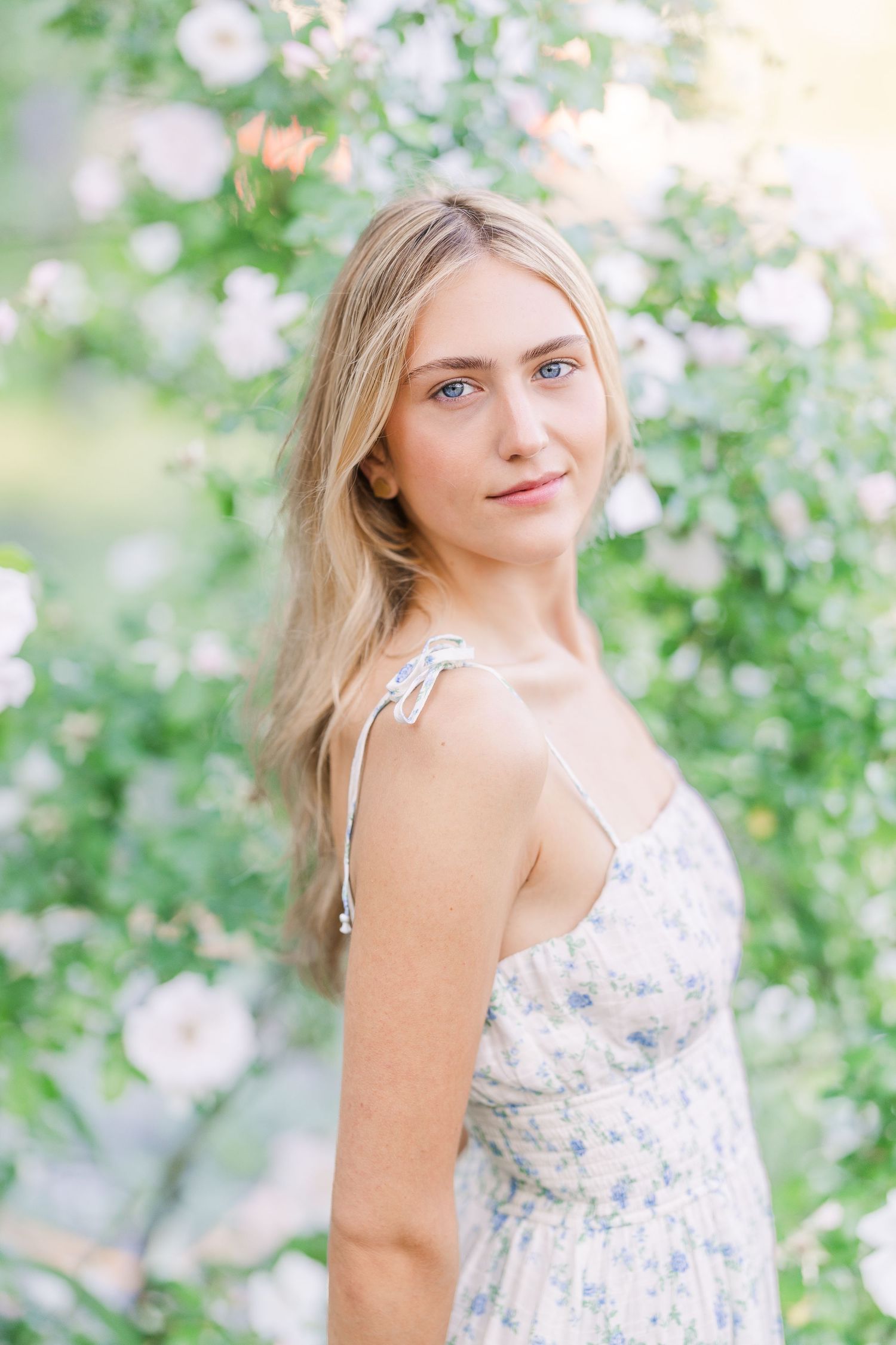 Light floral sundress photographed against blooming spring flowers in a dreamy garden setting.