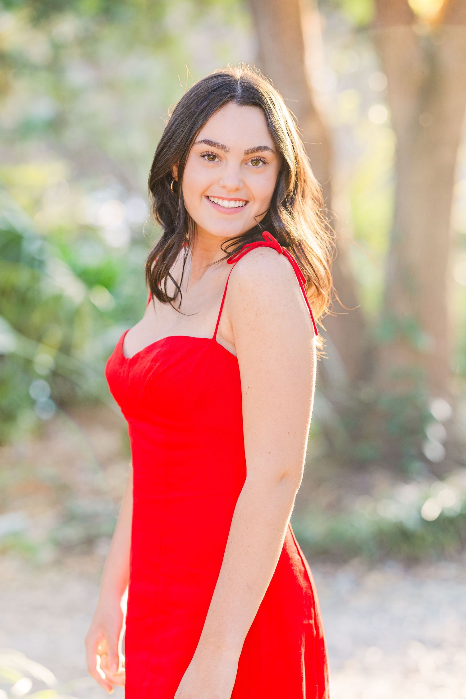 Natural light portrait with a bright red dress against a leafy background.