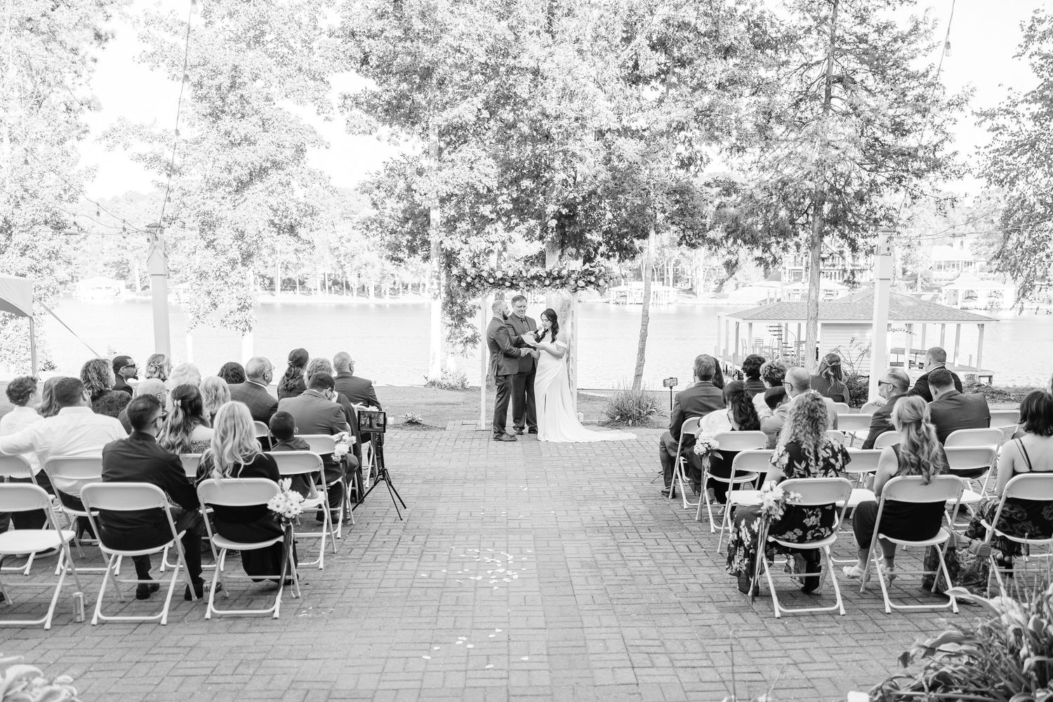 Wedding guests seated in white chairs on a lawn during an outdoor ceremony at sunset wedding groom bride lake Gaston photographer light airy