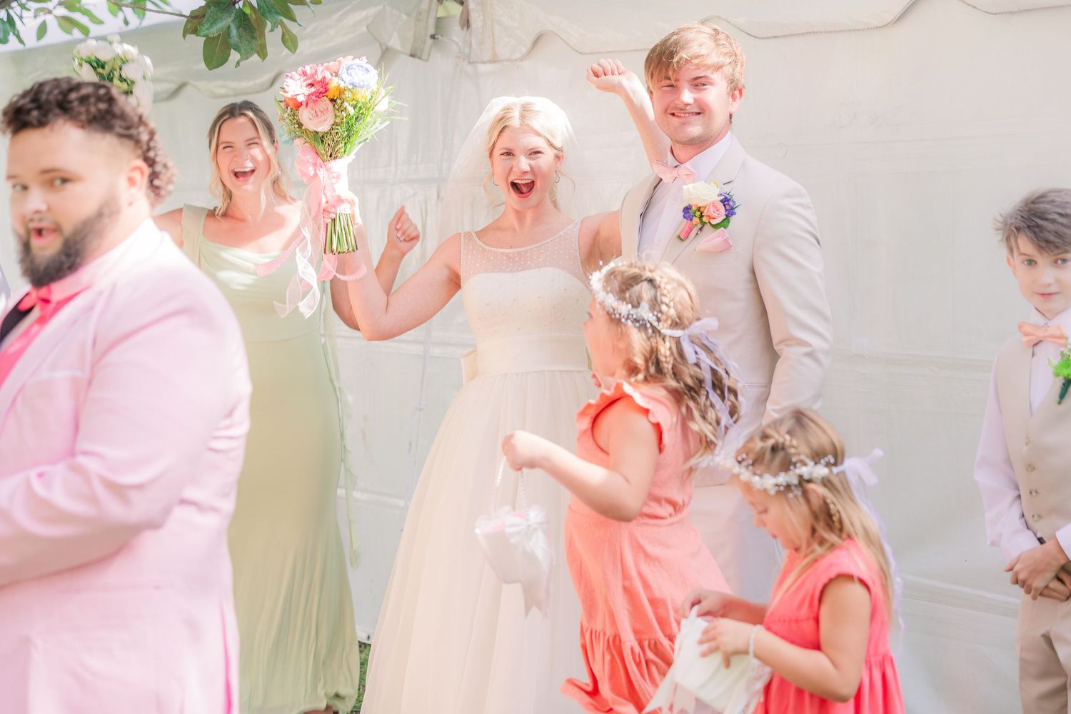 Wedding party celebrates joyfully under floral decorations with bridesmaids in coral dresses wedding groom bride wilmington photographer
