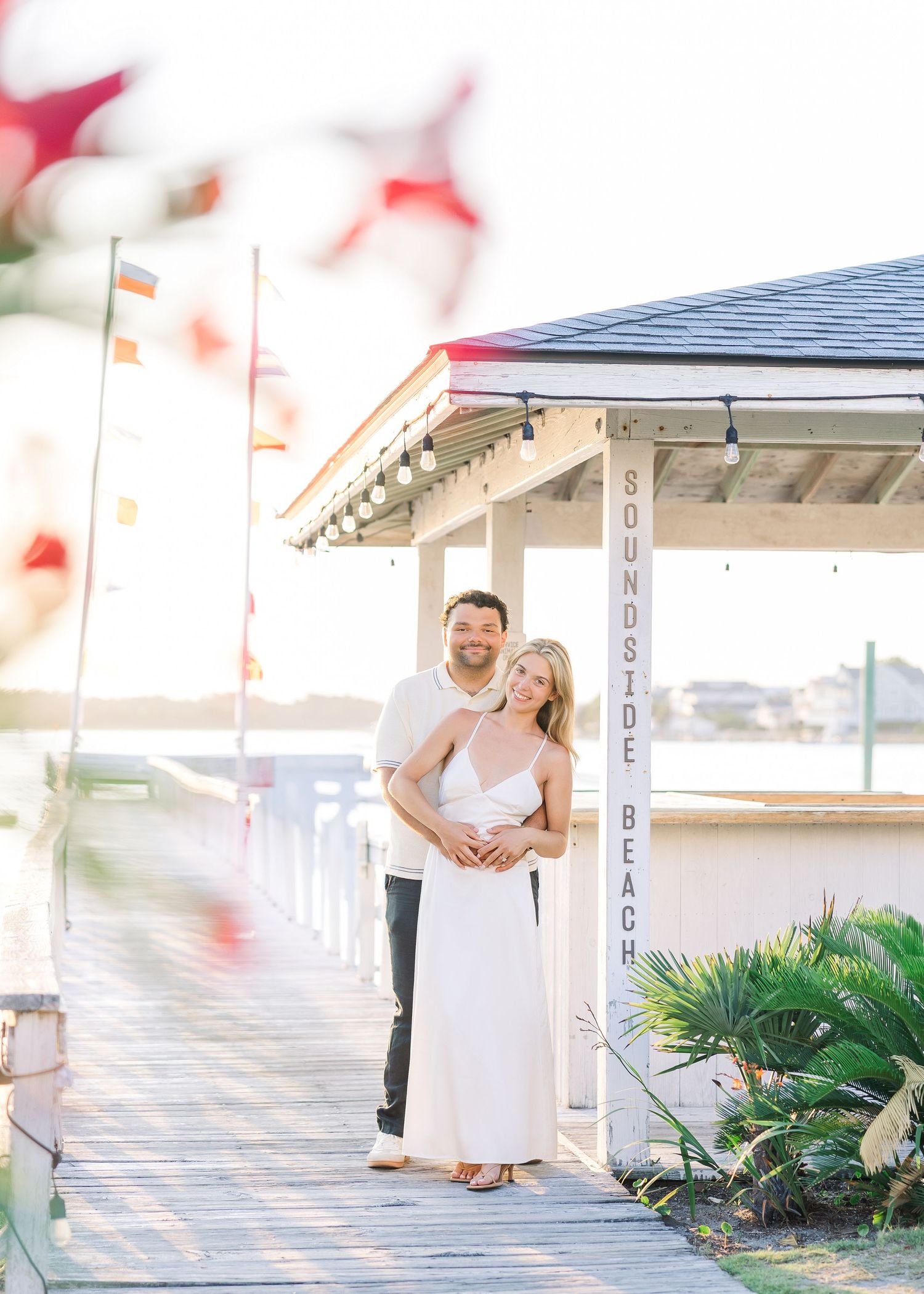 Happy couple embracing at Soundside Beach dock, woman in white dress, bathed in warm sunset light.