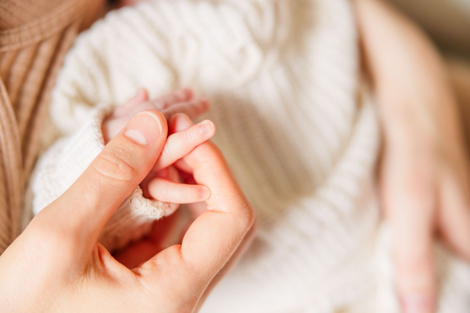 Tender close-up of baby's tiny fingers being held against soft white fabric.