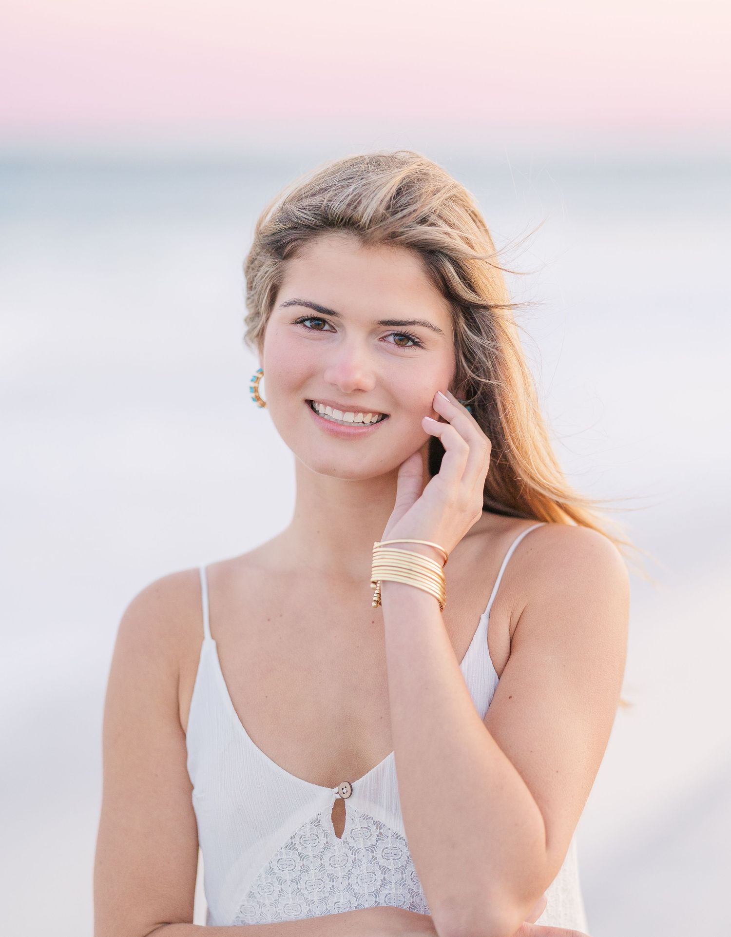 Close-up portrait with soft lighting and delicate jewelry against a beach backdrop.