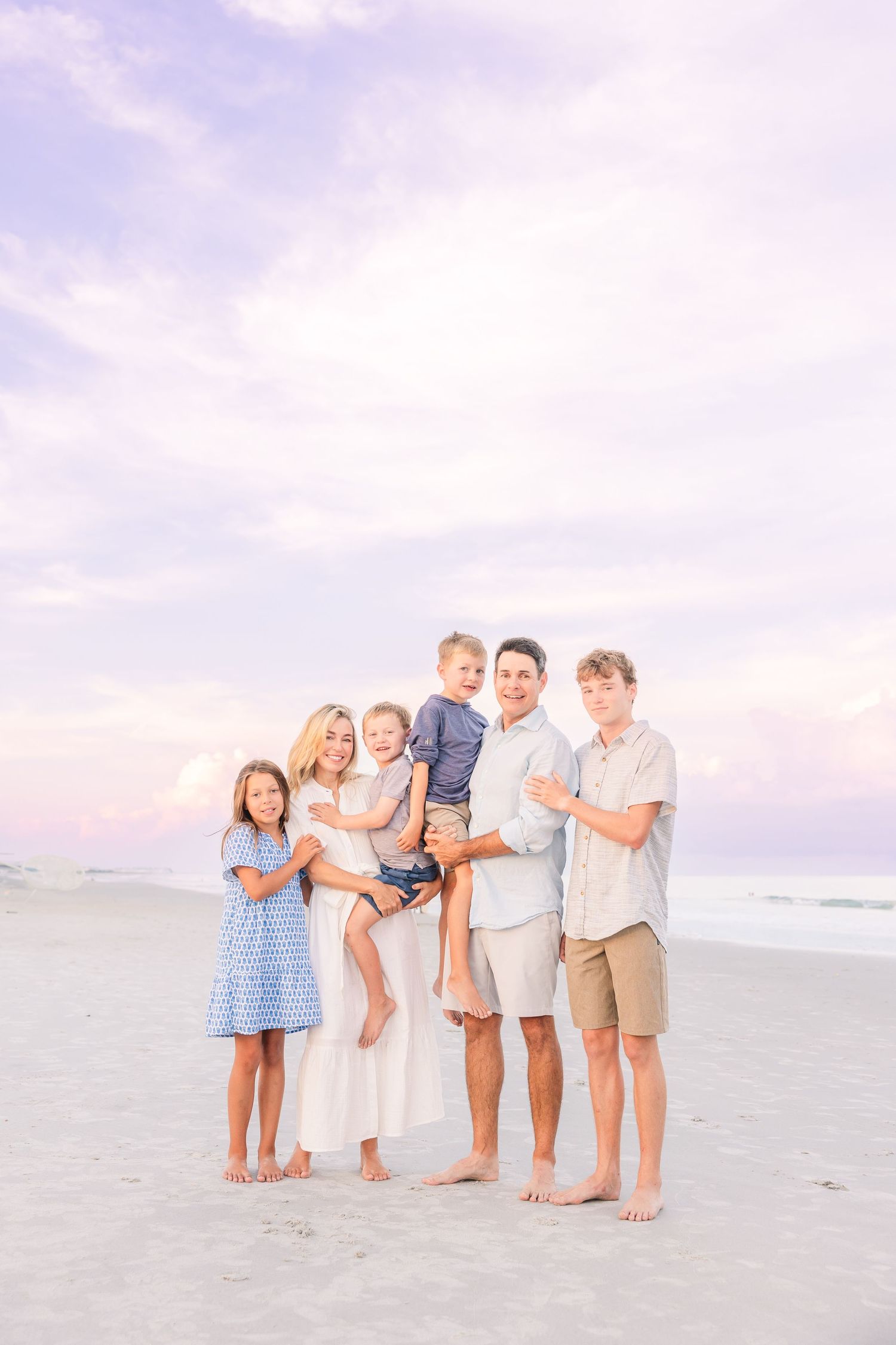 Family standing together on beach with pastel purple sky and ocean view.