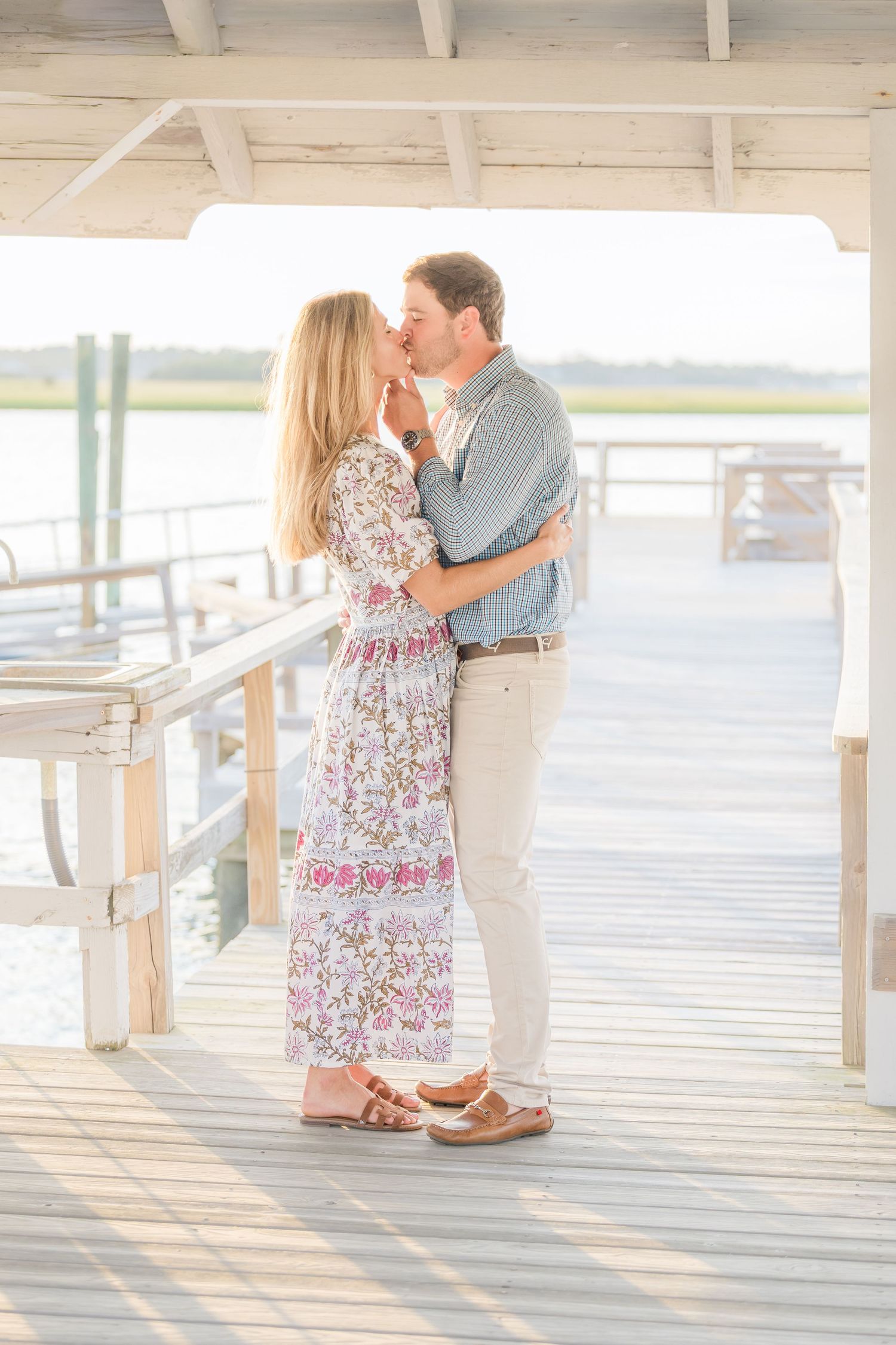 A tender moment between a couple on a covered waterfront boardwalk in summer attire.