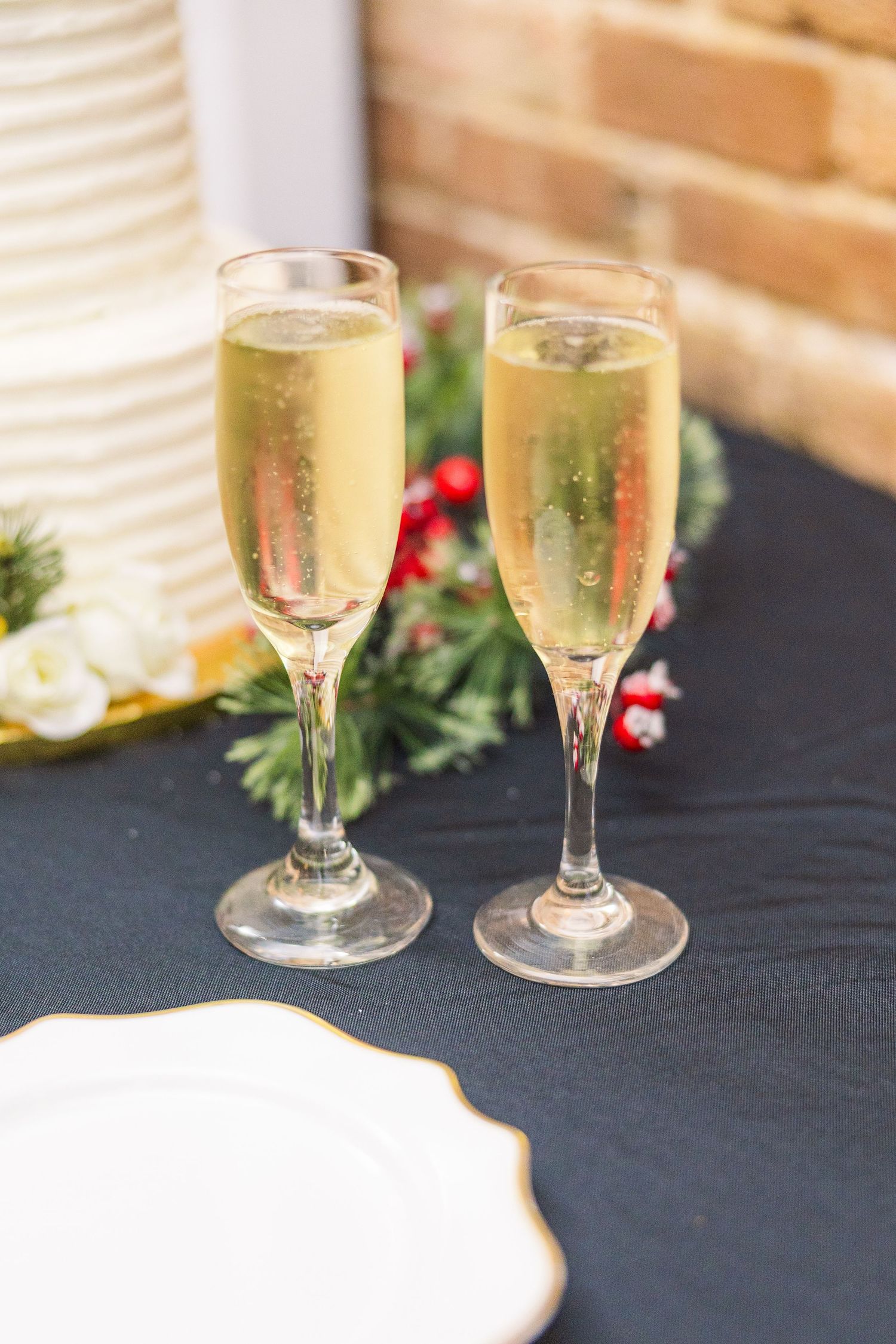 Two champagne flutes with bubbly on a dark tablecloth with holiday greenery wedding groom bride wilmington North Carolina photographer light