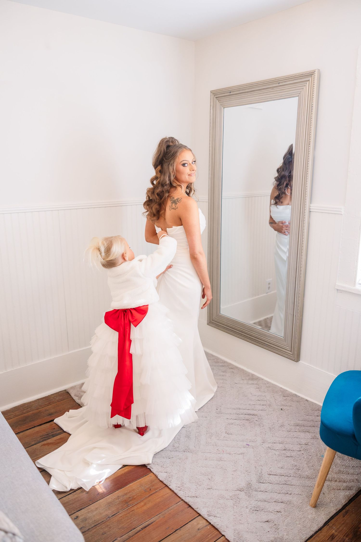 Wedding dress preparation with a red accent bow visible in the mirror reflection.
