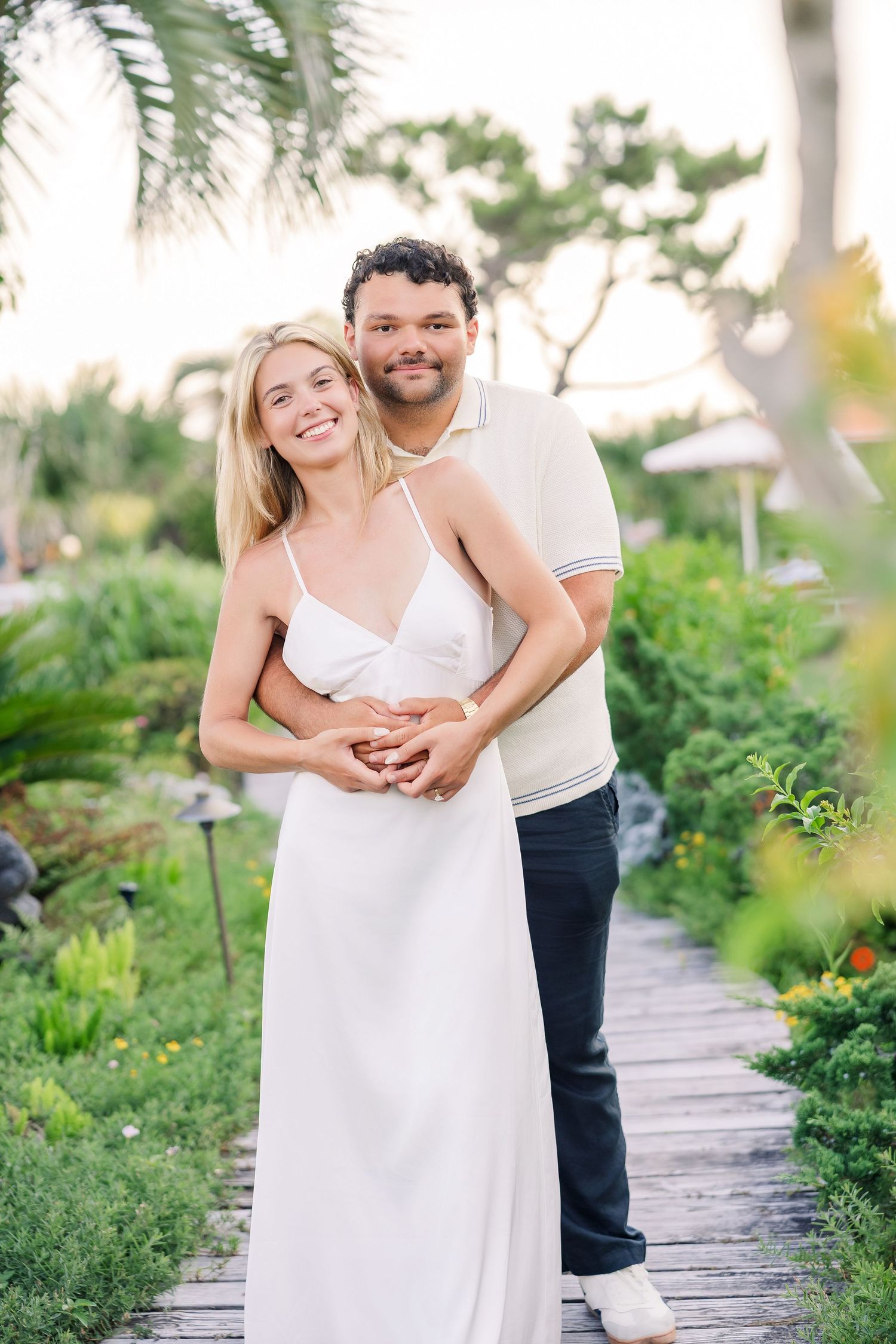 Happy couple embracing on a wooden path in a tropical garden at sunset.