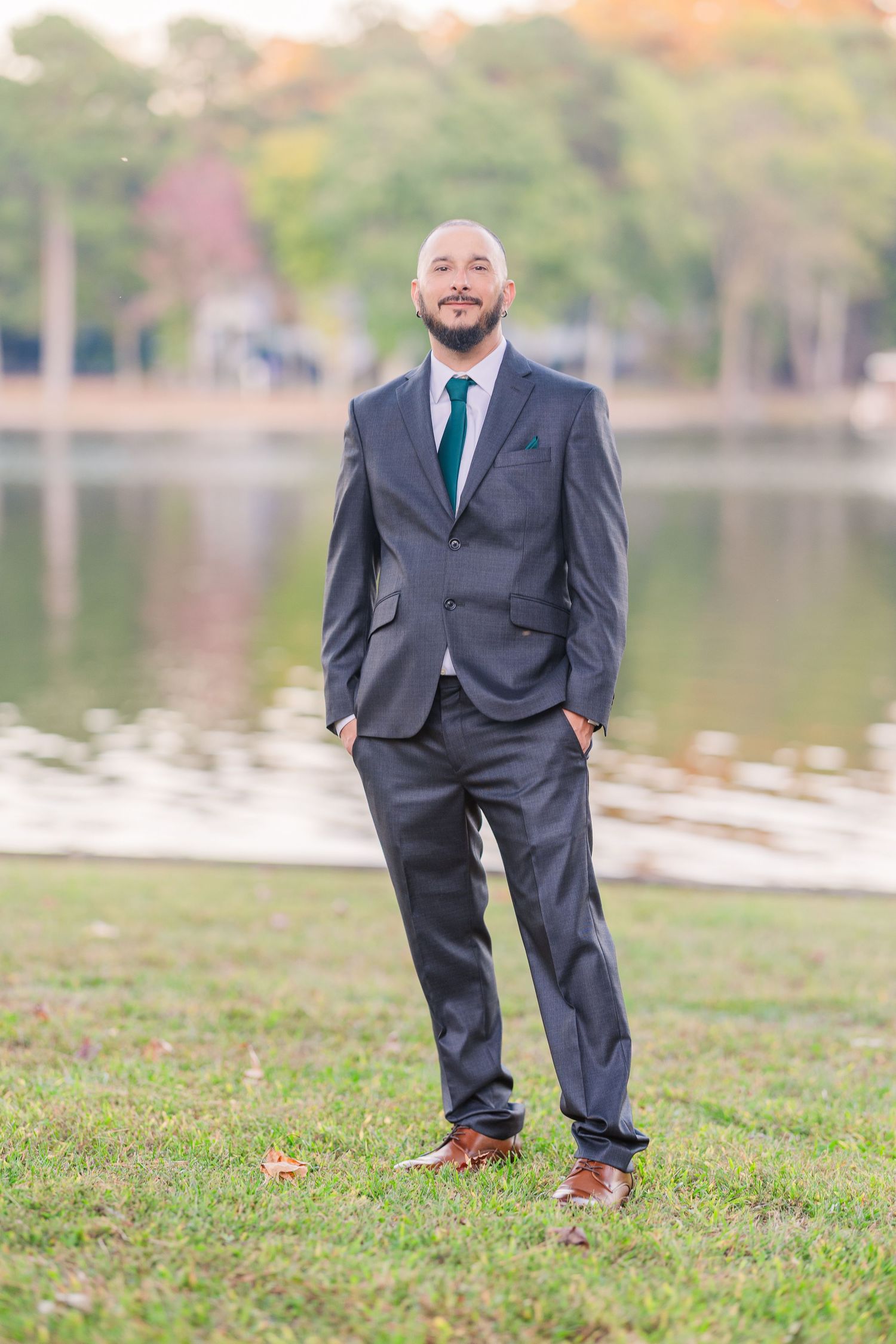 Groom in dark suit and teal tie poses on grassy lawn near lakefront wedding groom bride lake Gaston photographer light airy