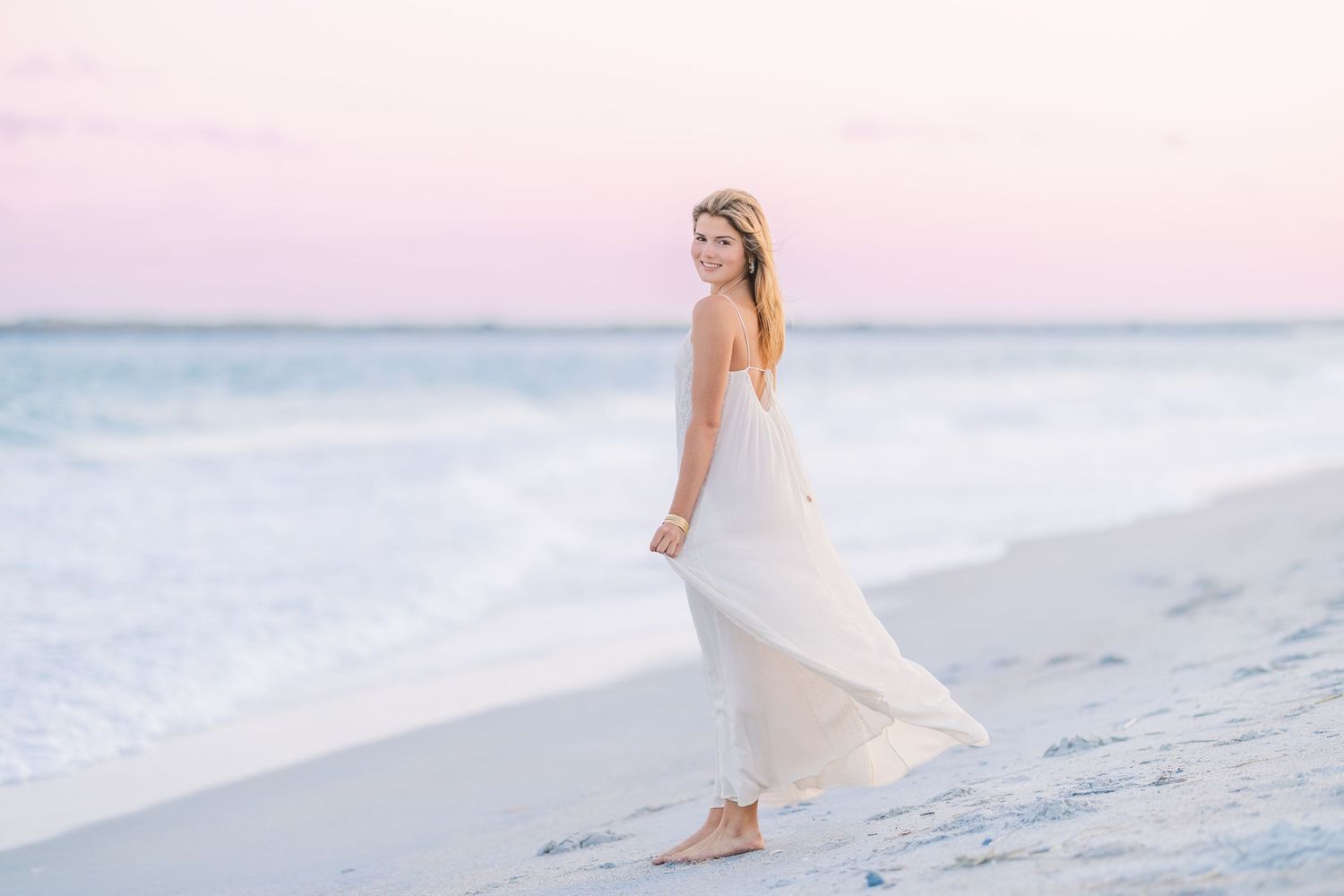 Ethereal beach scene with flowing white dress against pastel sunset sky and ocean waves.