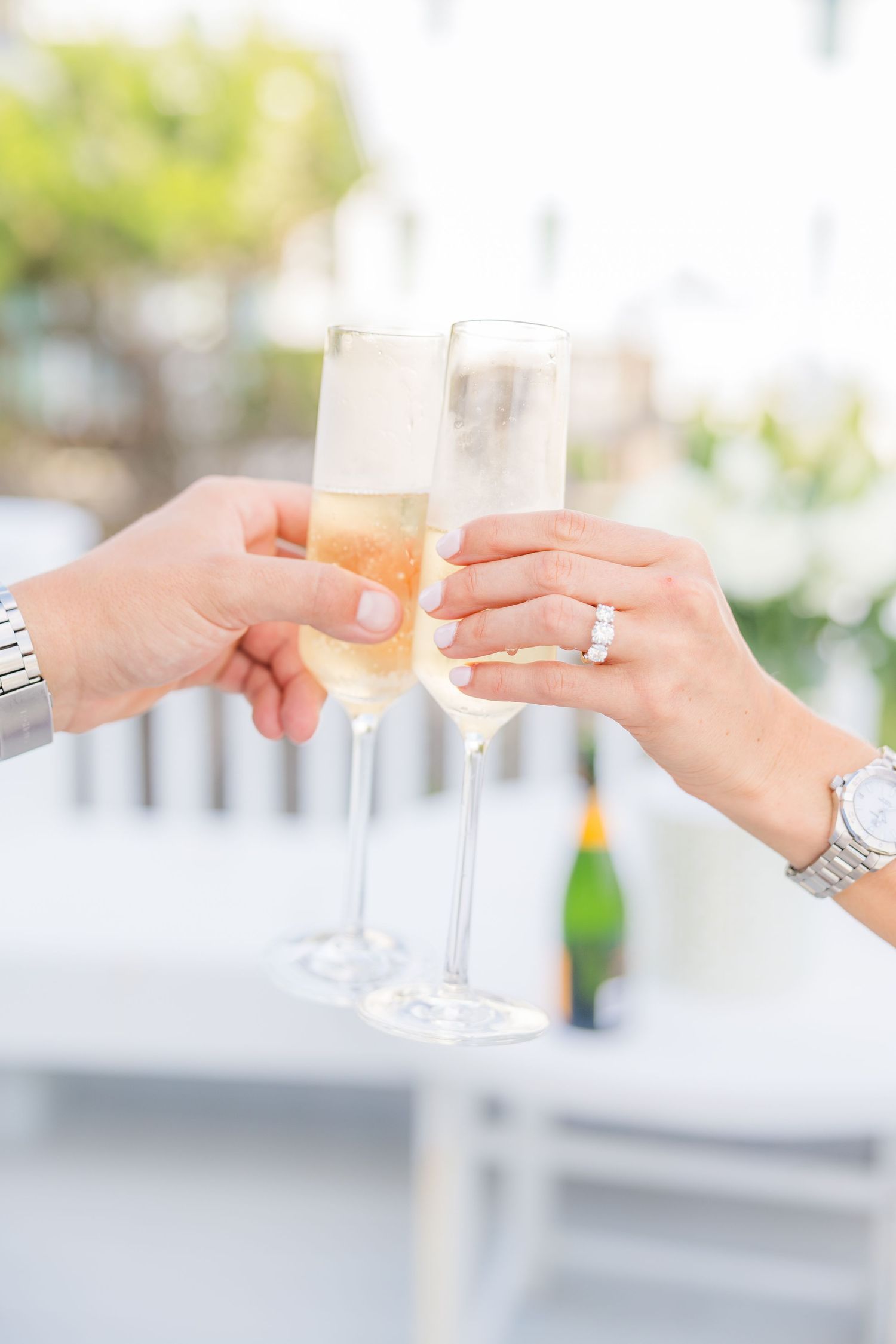 Champagne glasses clink together in a celebratory toast on a bright porch.