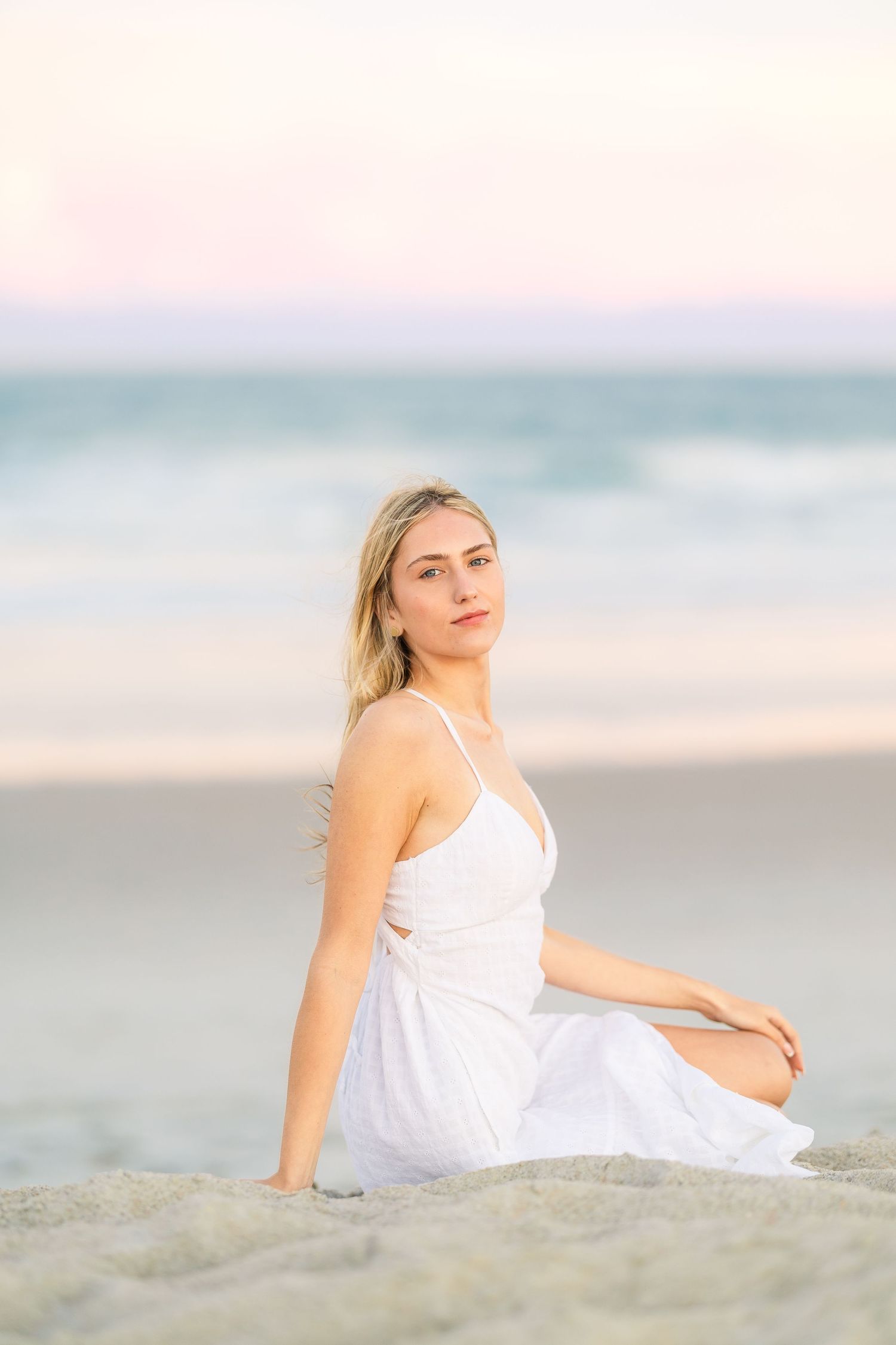 Relaxed beach portrait with subject reclining on sand in white dress.