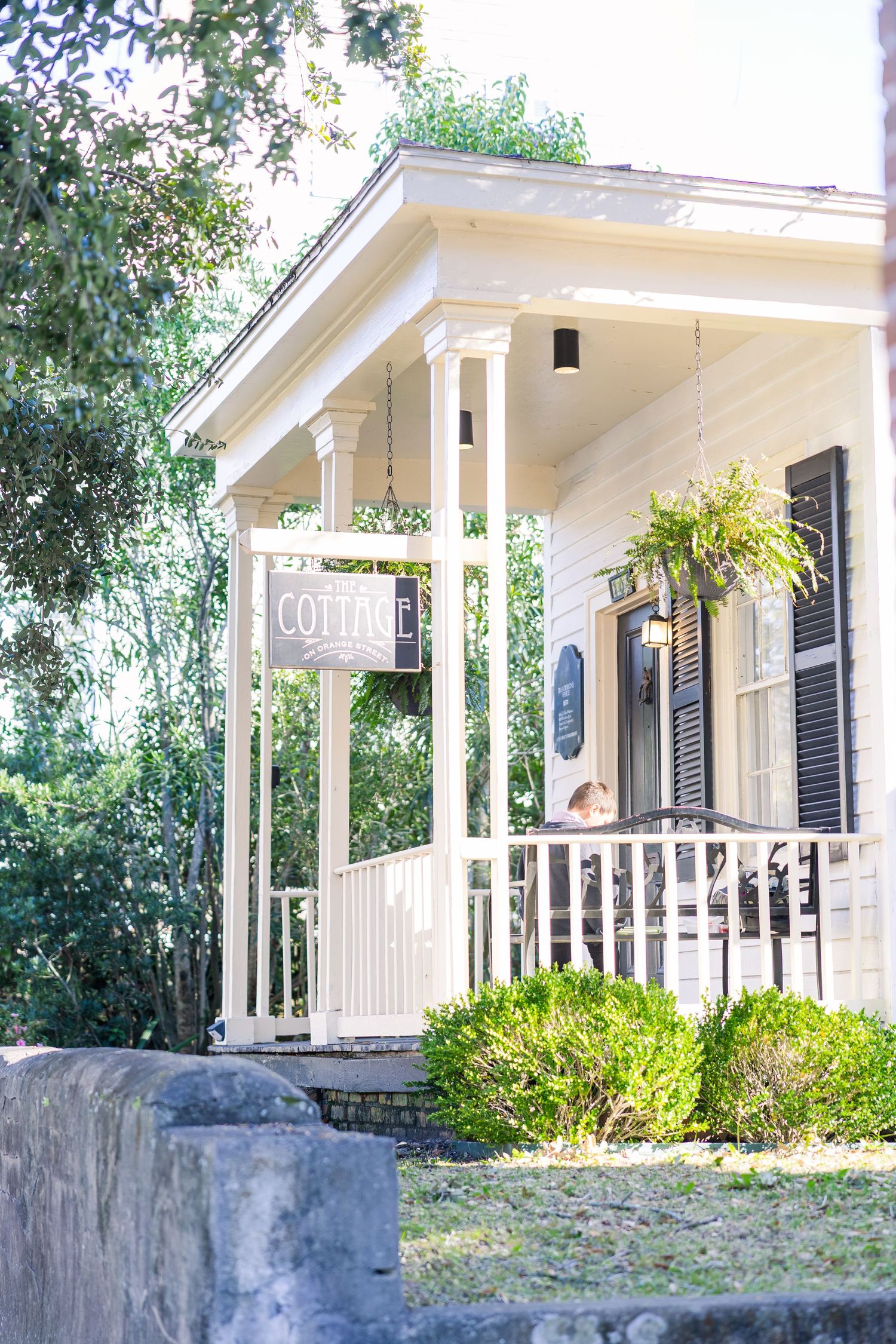 A charming white cottage venue with wraparound porch and black shutters.