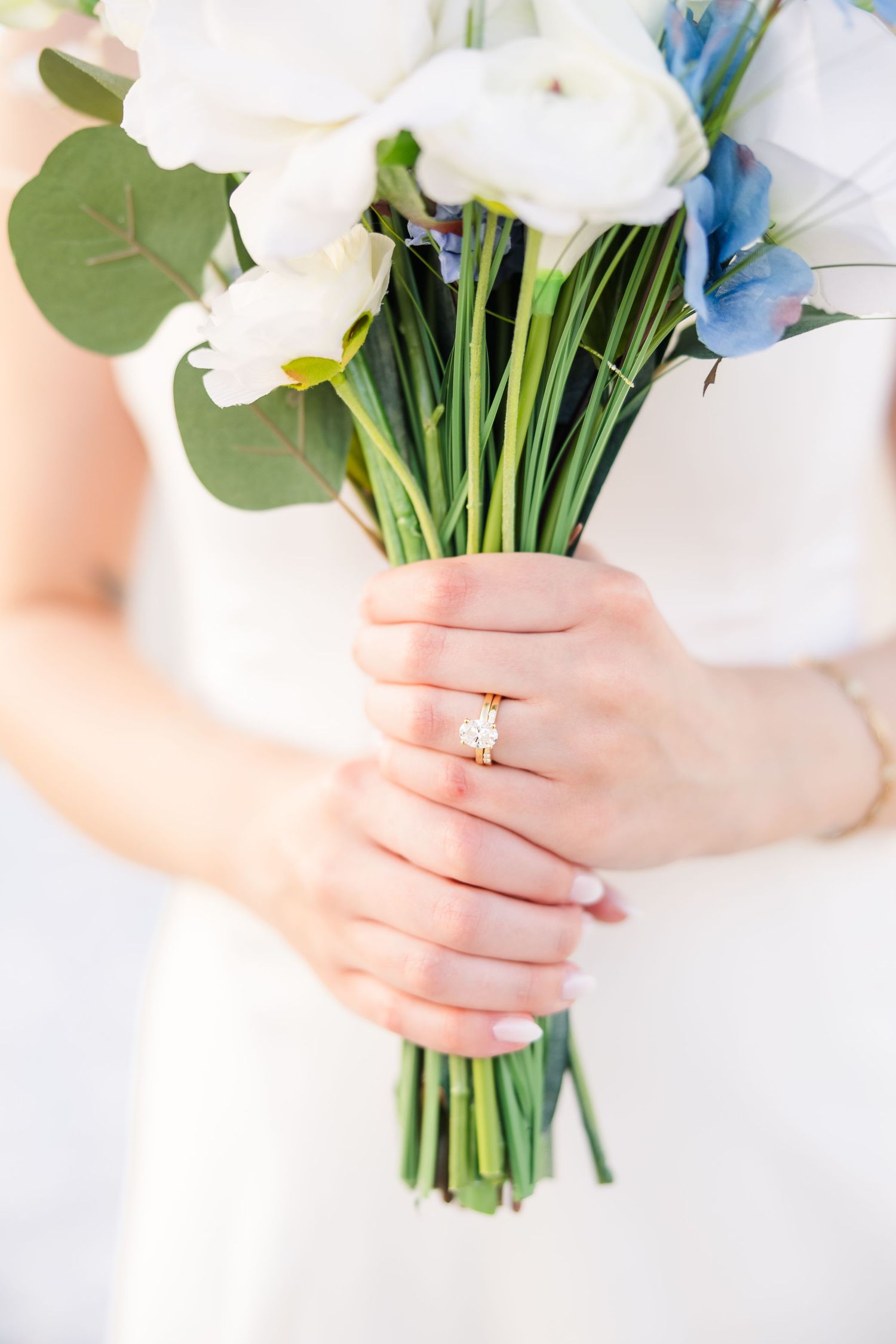 Bride holding a white and blue floral bouquet with a gold diamond engagement ring on her finger in Carolina Beach near Wilmington, NC.