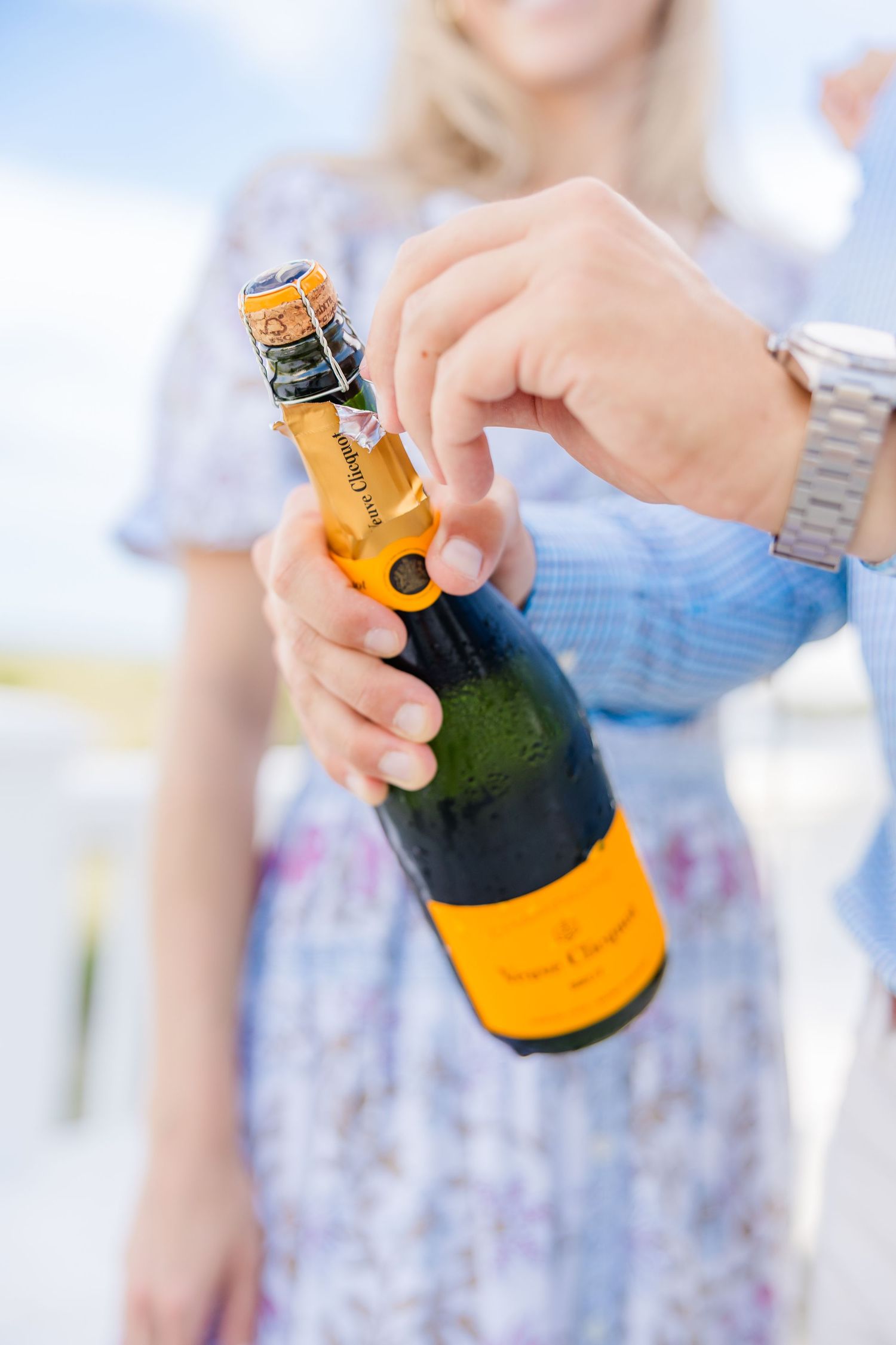 Hands hold a yellow-labeled champagne bottle during an outdoor celebration.
