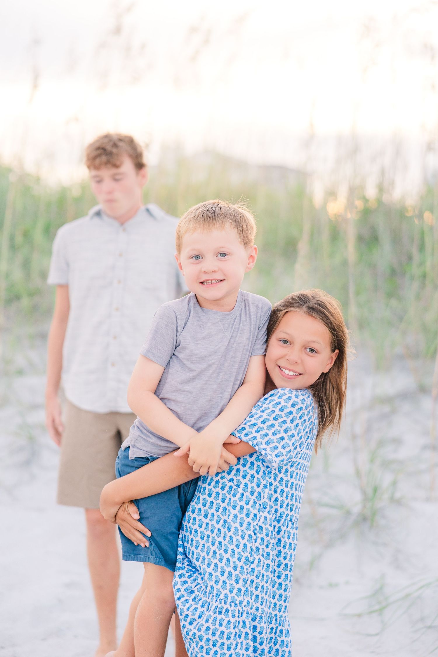Children in coordinated outfits playing and laughing on beach sand dunes.