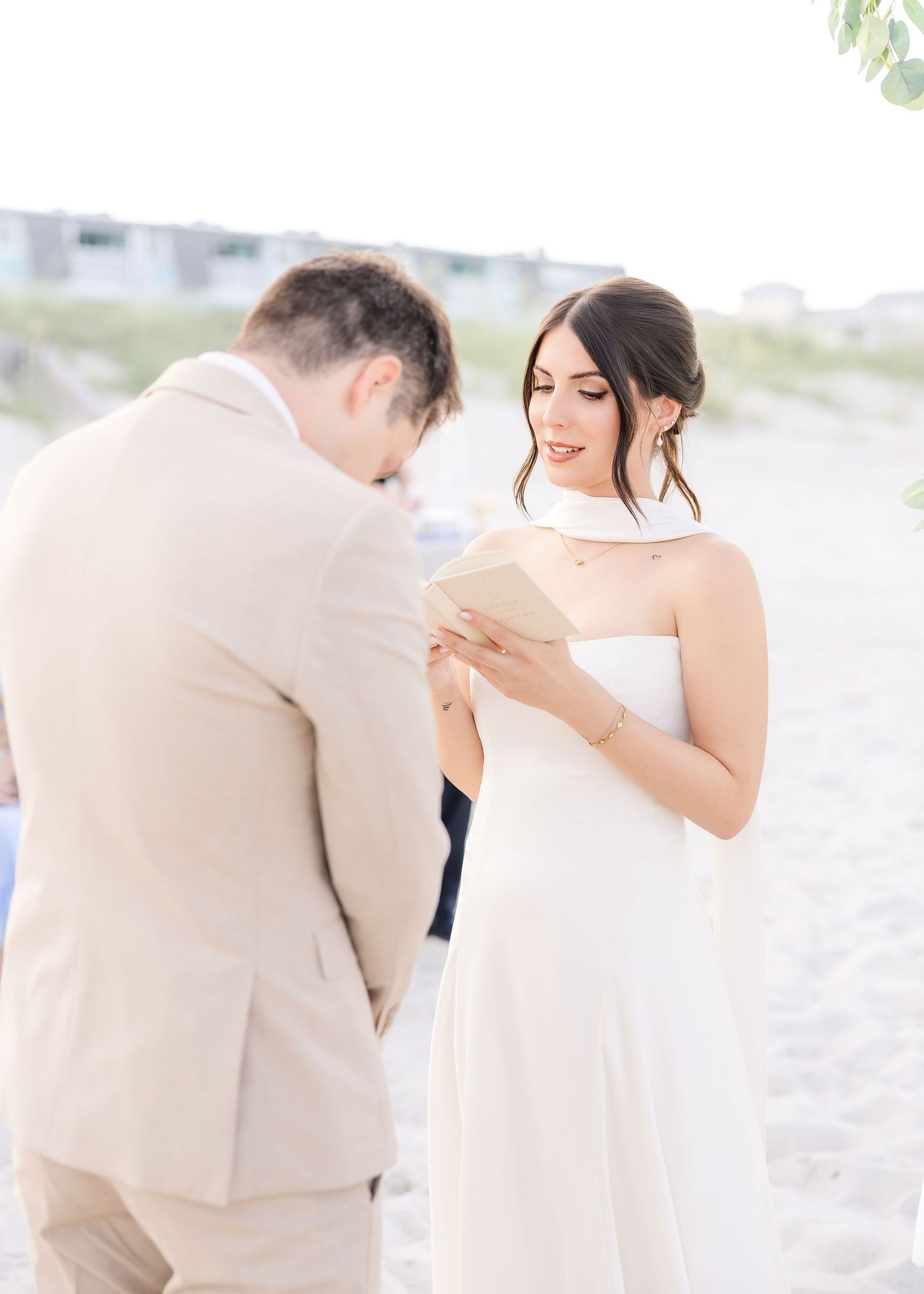 Bride reads vows from a card during an intimate beach wedding ceremony while groom listens attentively in Carolina Beach near Wilmington, NC