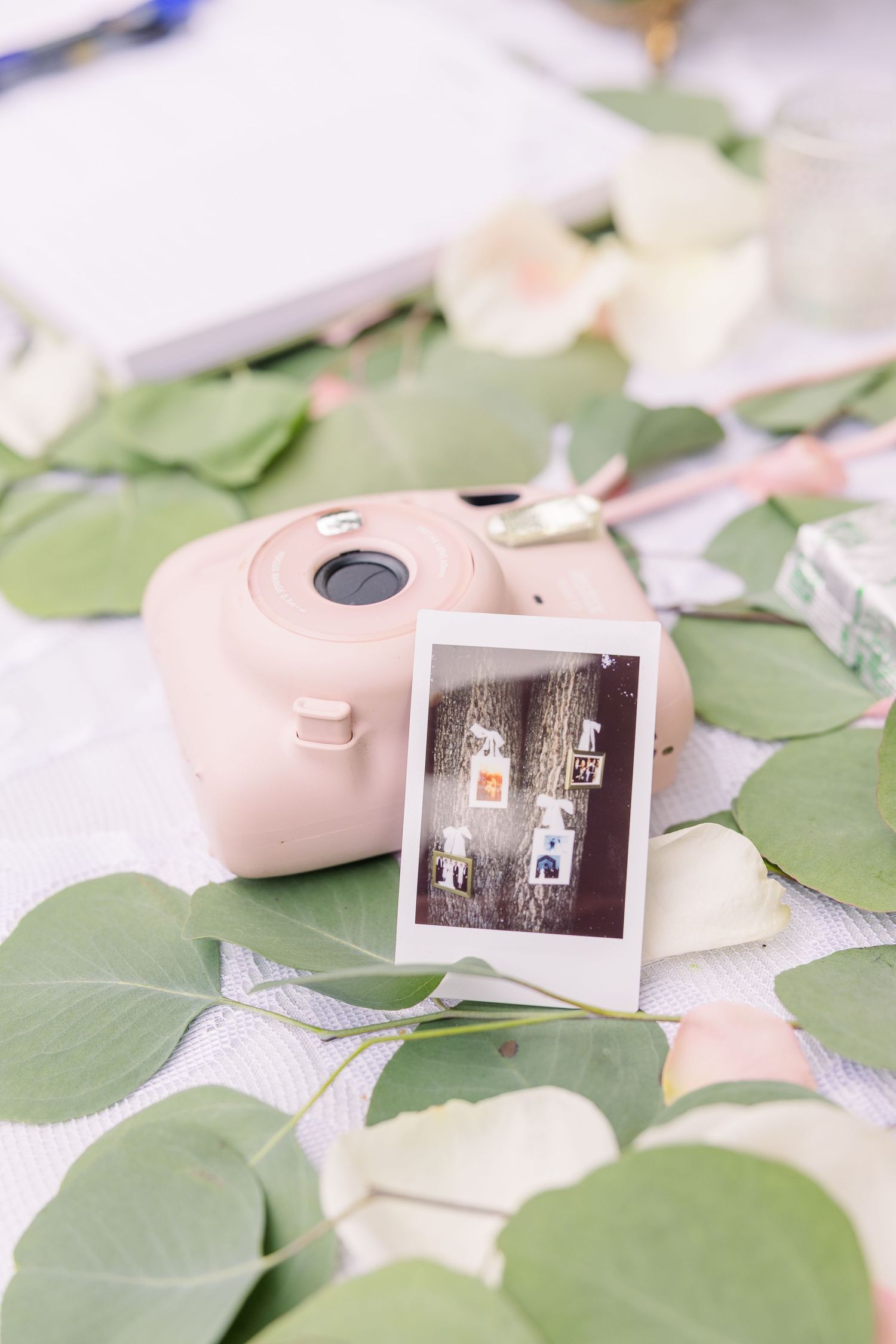 Vintage-style instant photos scattered among green eucalyptus leaves on white surface wedding groom bride wilmington North Carolina