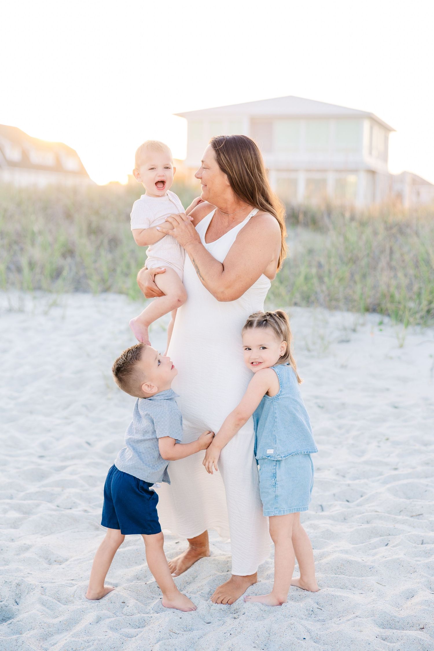 Grandmother holding a baby while two young children hug her on a sunny beach.