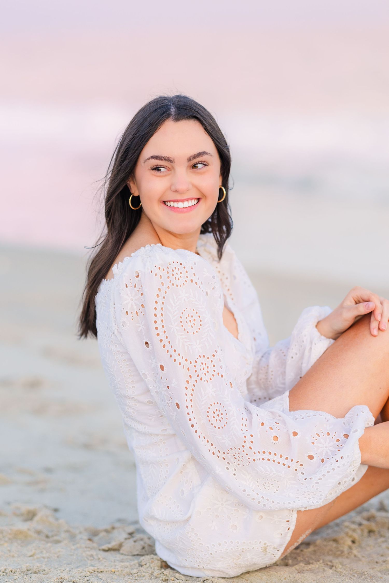 Casual beach portrait featuring white eyelet dress and natural sunset lighting.
