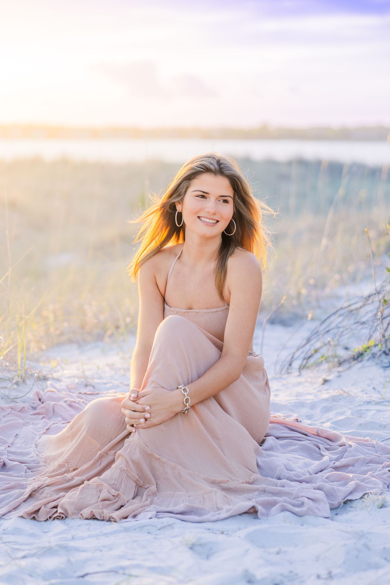 Romantic beach photography session with soft pastel tones and flowing fabric against white sand.
