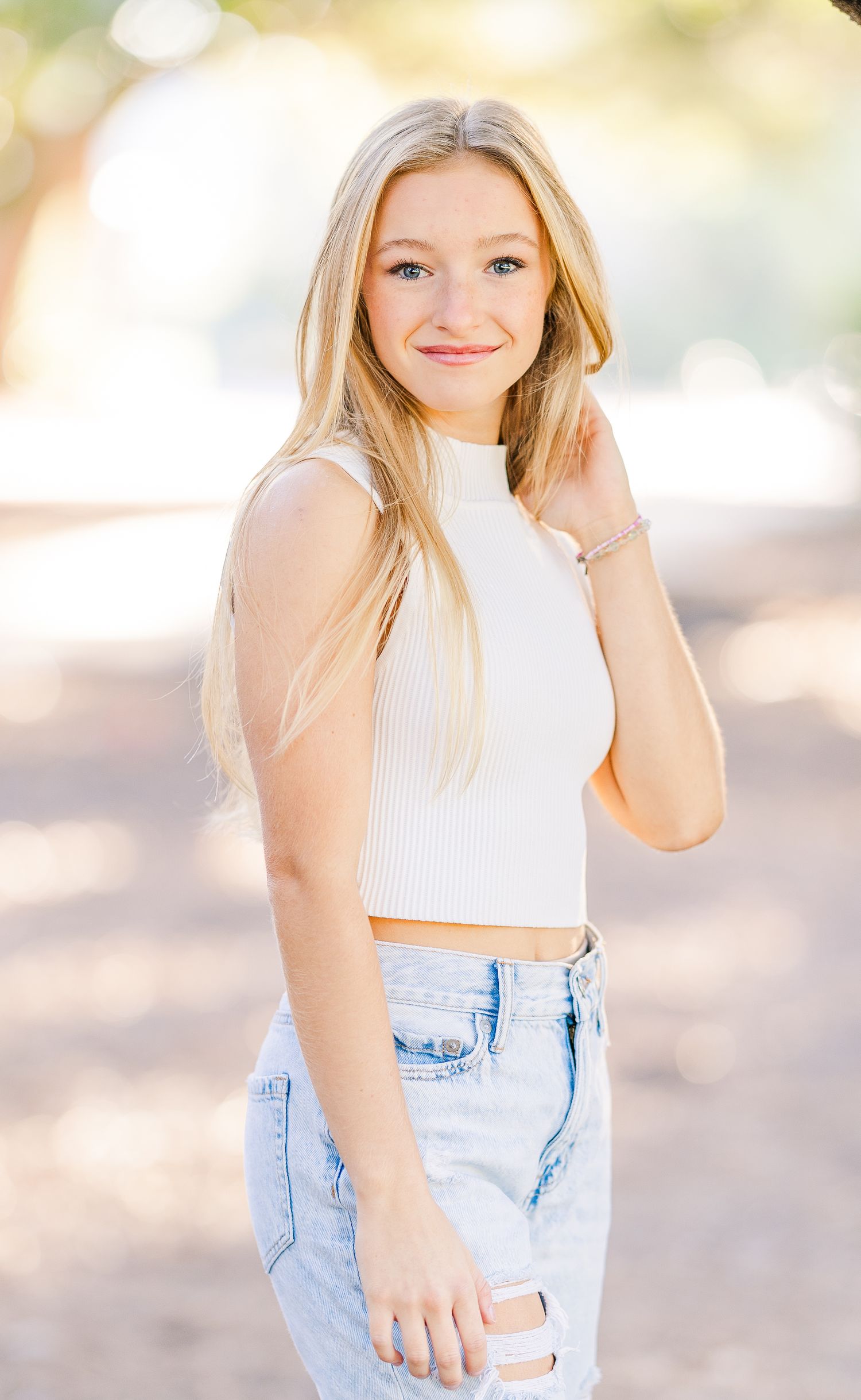 A college UNCW senior wearing a white crop top and light blue denim poses outdoors in natural lighting for a portrait in Wilmington.