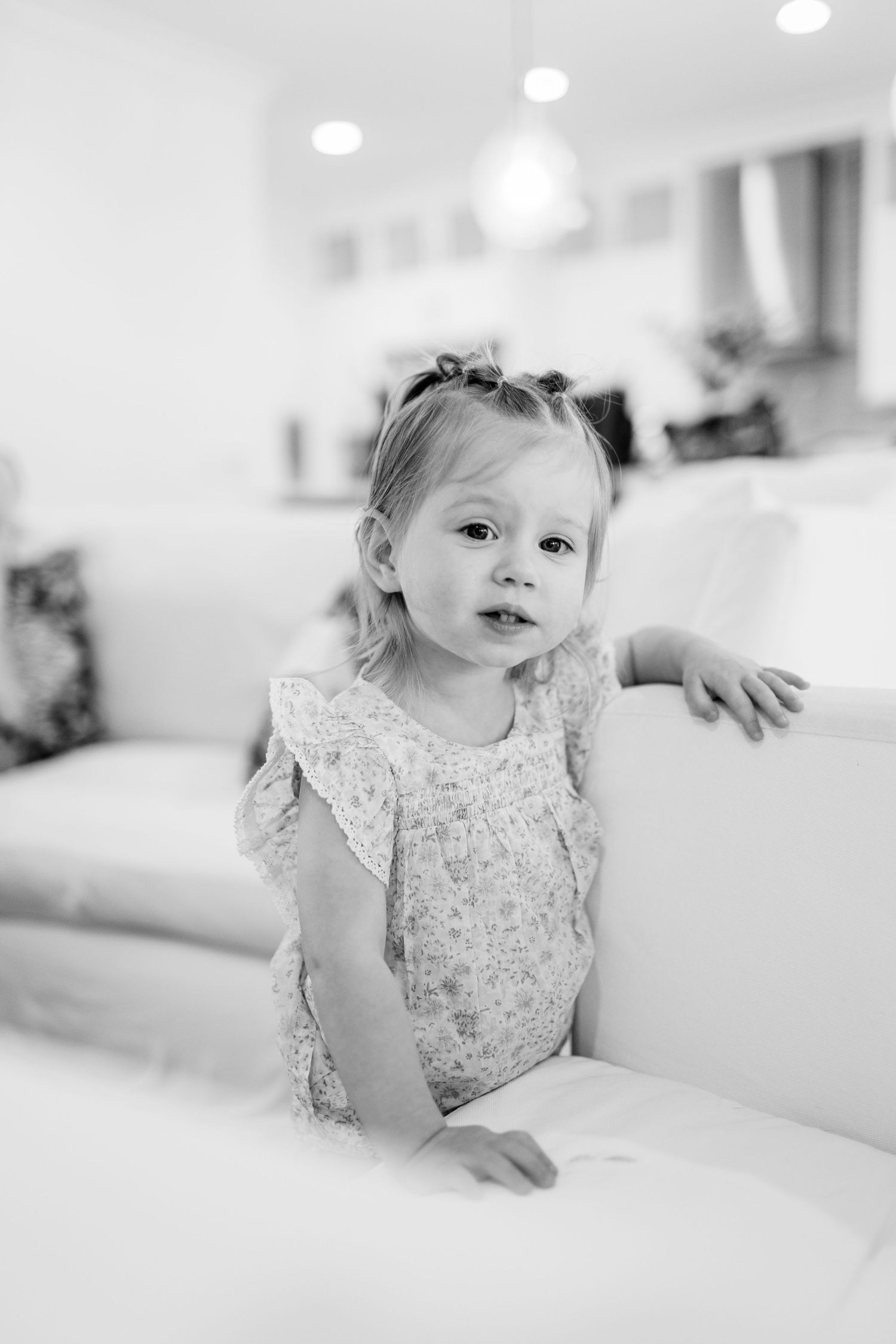 Child in white lace dress poses on white couch in natural light.