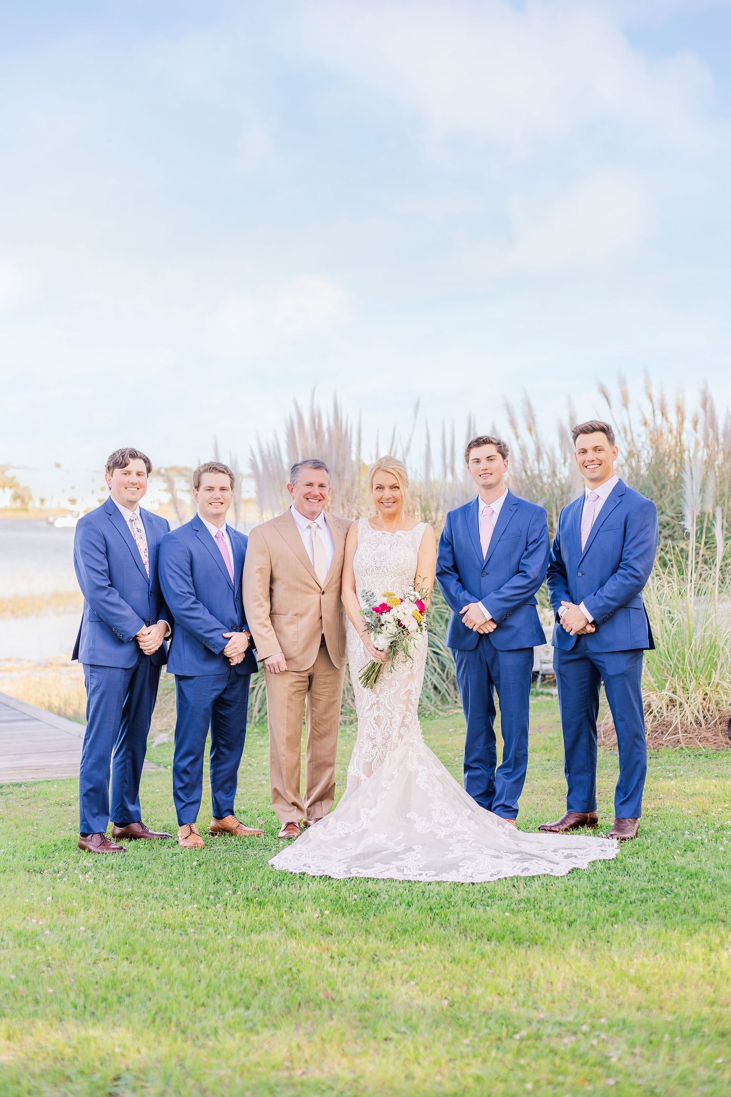 Wedding party in blue suits and tan suit pose together waterfront landfall wedding bride groom light and airy classic wilmington Wrightsvill