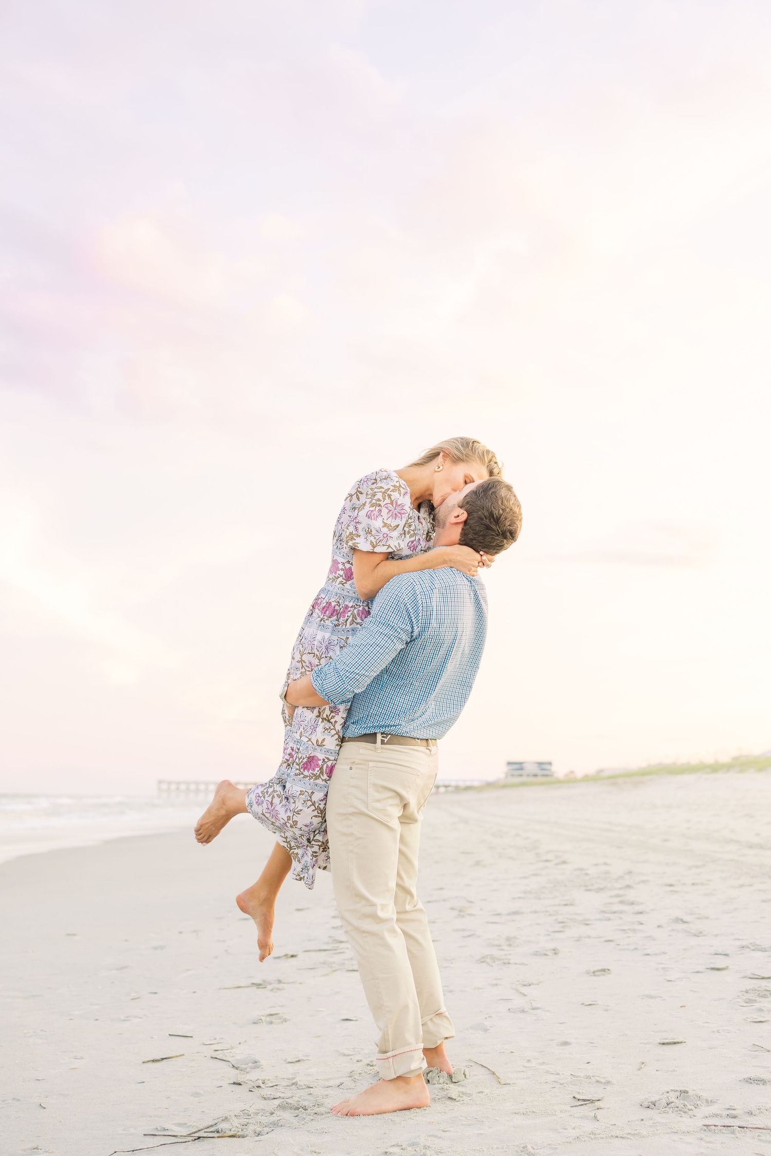 Couple sharing an intimate moment on the beach with soft pink sky in background.