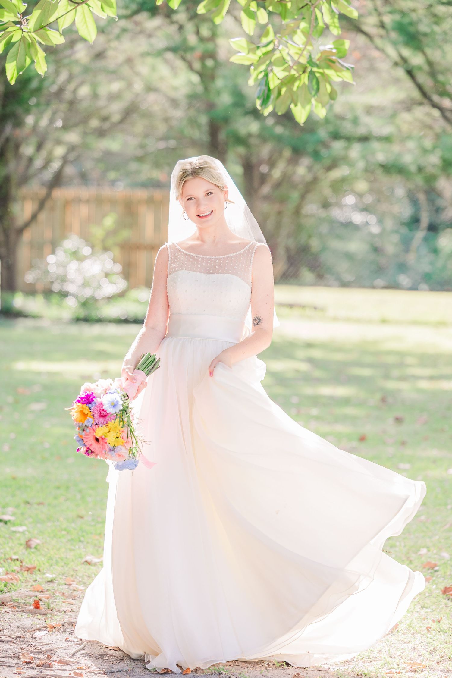 A bride spins in her white ballgown dress under sunlit trees in a garden setting.