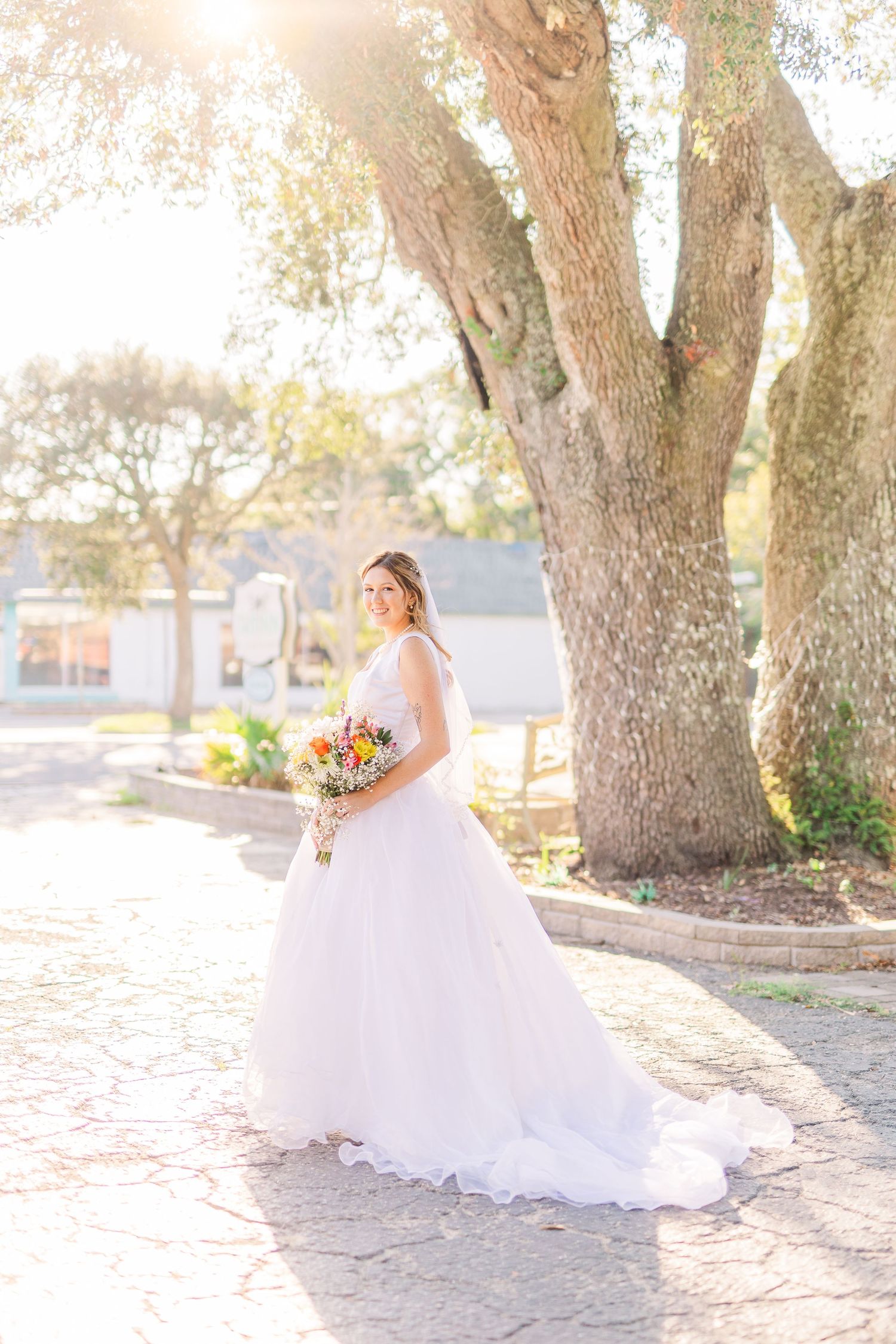 Bride in white dress holds bouquet while posing under sunlit trees southport elopement wedding bride groom light and airy classic