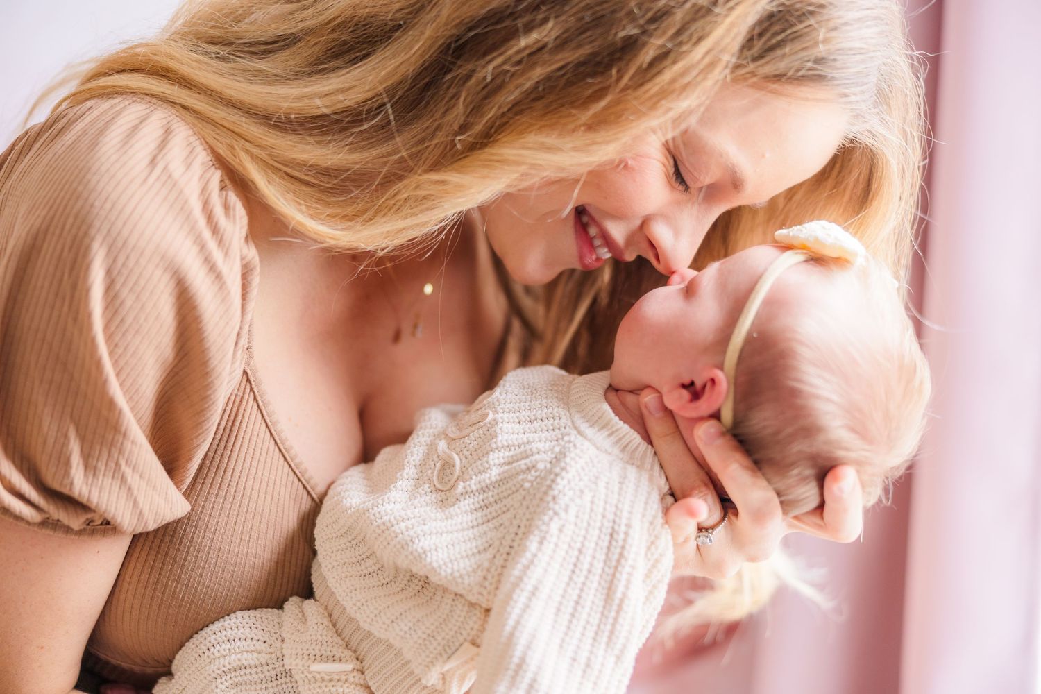 Loving embrace between parent and baby against pink wall.