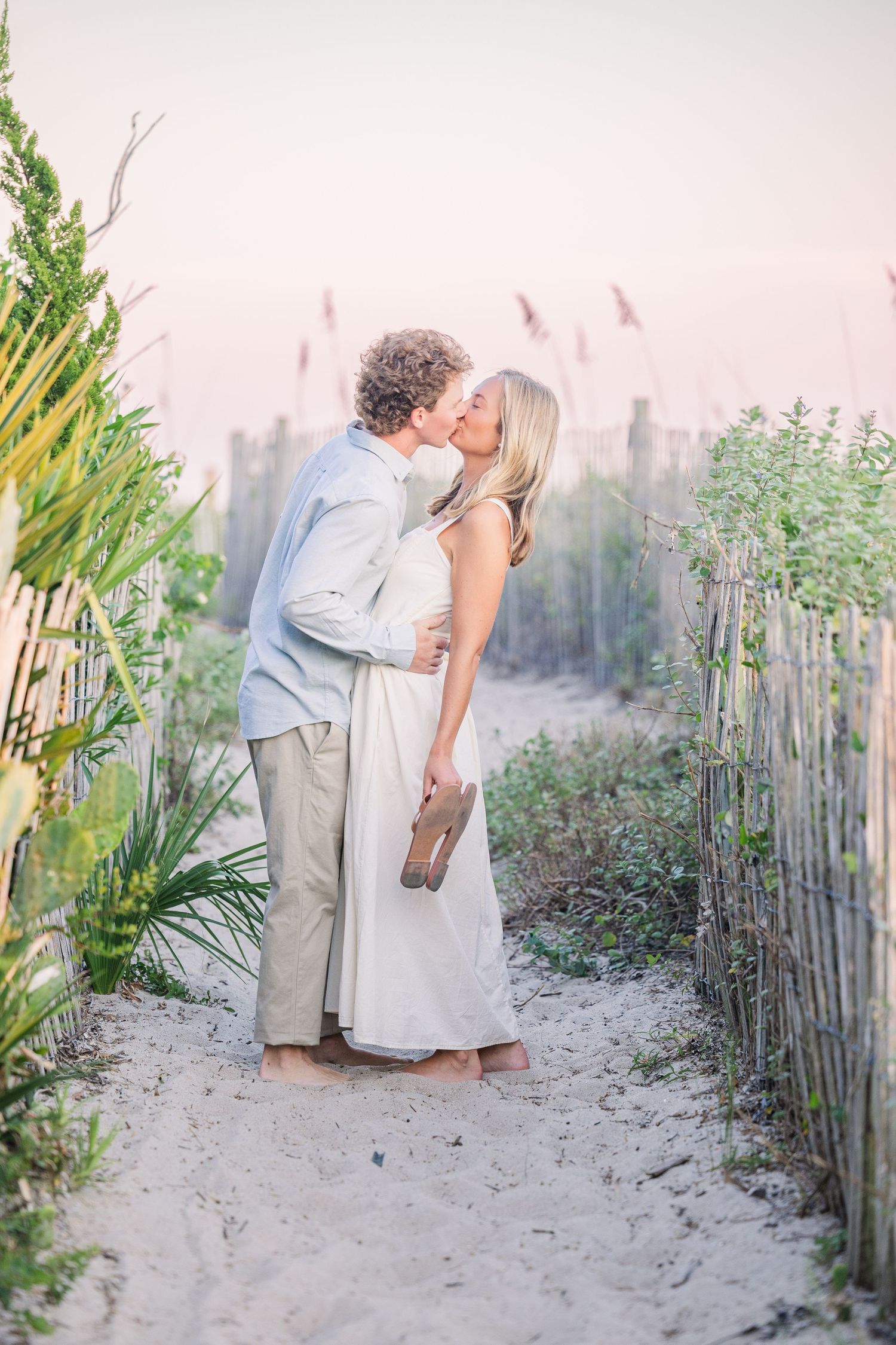 Couple sharing intimate moment along wooden fence pathway on sandy beach.