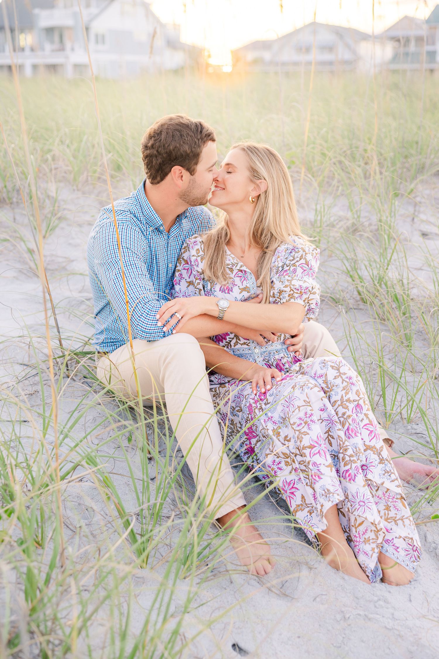 Couple sitting together in beach grass during golden hour by the ocean.